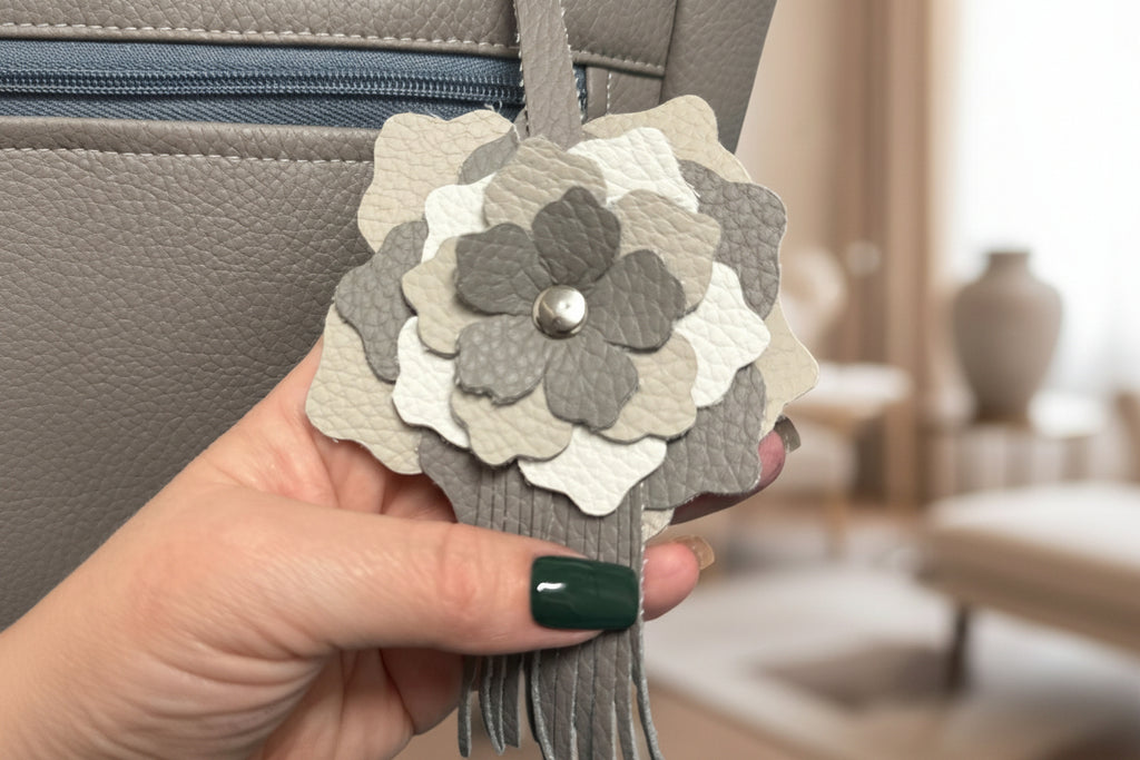 Hand holding a gray and white floral keychain with a blurred indoor background