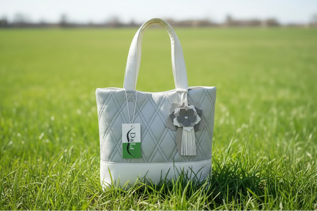 Quilted pattern handbag with a decorative flower and tag on grass