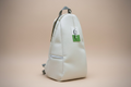 White backpack with a green label on a wooden bench in a park