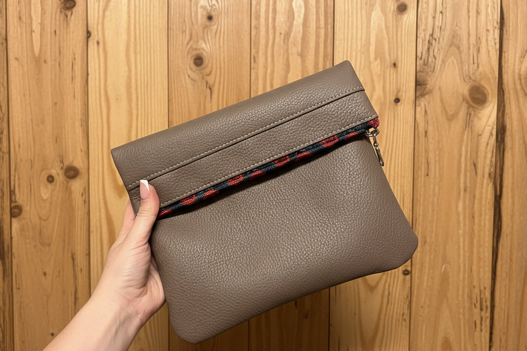 Hand holding a brown cosmetic bag against a wooden background