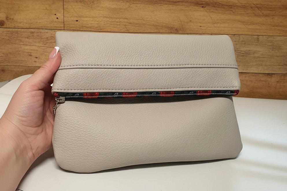 Beige cosmetic bag with a zipper held by a hand on a white background