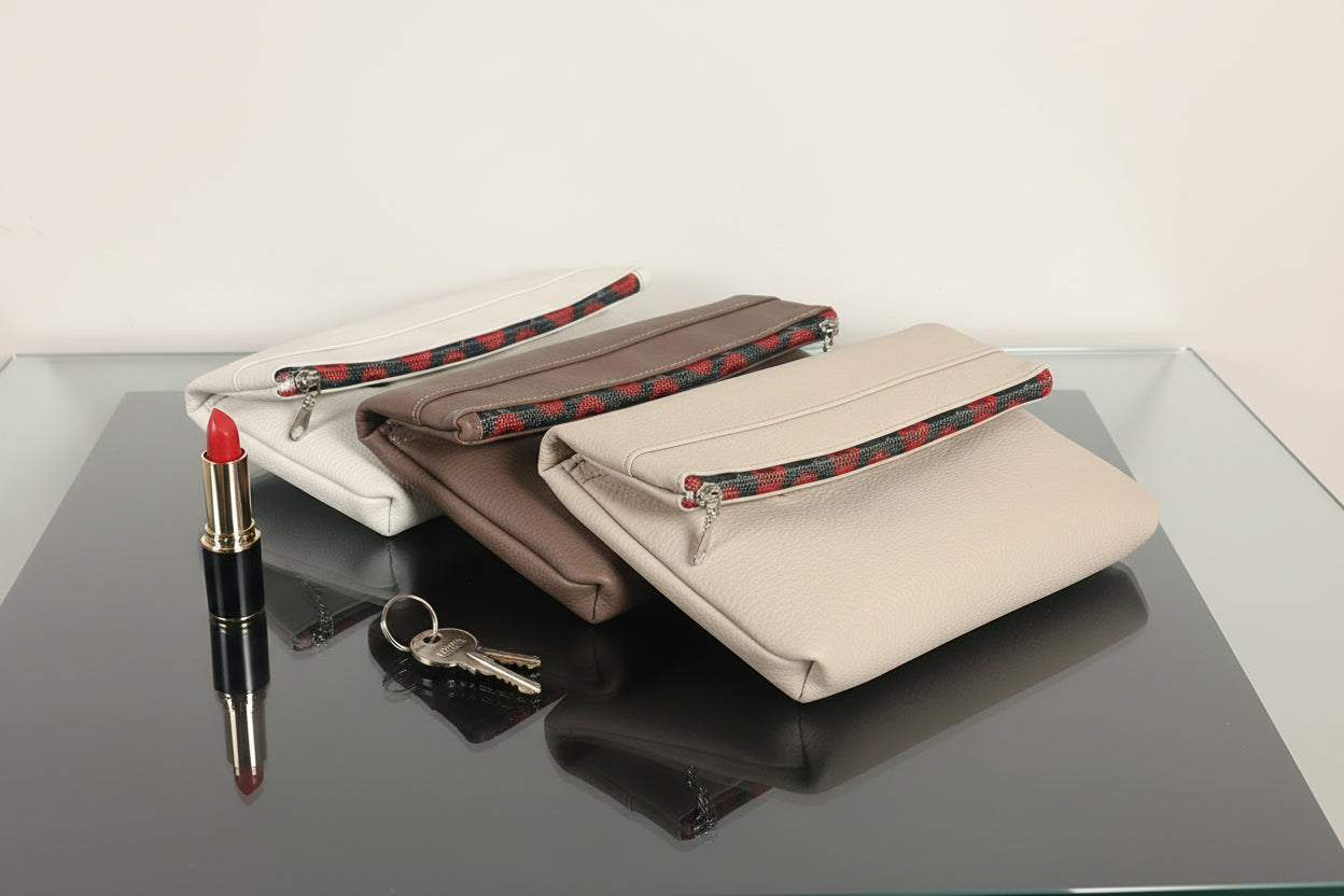 Set of three cosmetic bag on a reflective surface with a lipstick and keys beside them.