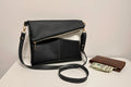 Black faux leather handbag with a wallet and money on a light surface.