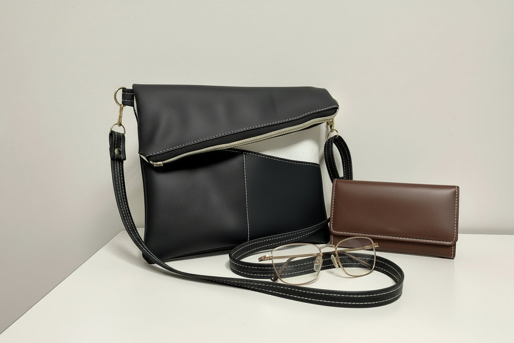 Black faux leather handbag with a brown wallet and glasses on a light surface.
