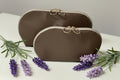 Two brown cosmetic bags with gold zippers on a white surface with lavender flowers.