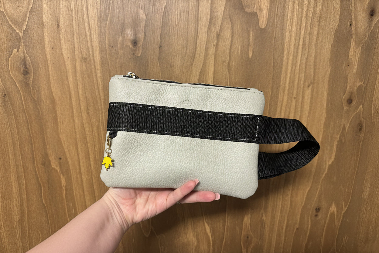 White wrist bag with a black strap held by a hand against a wooden background