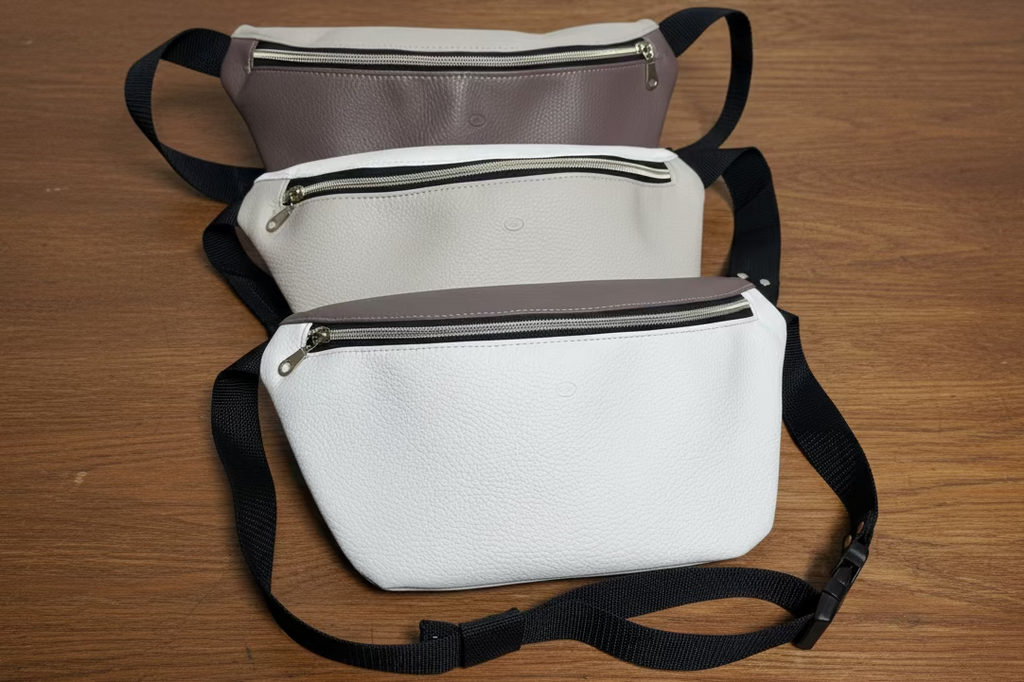 Three waist bags in white, gray, and brown with zippers on a light gray background.
