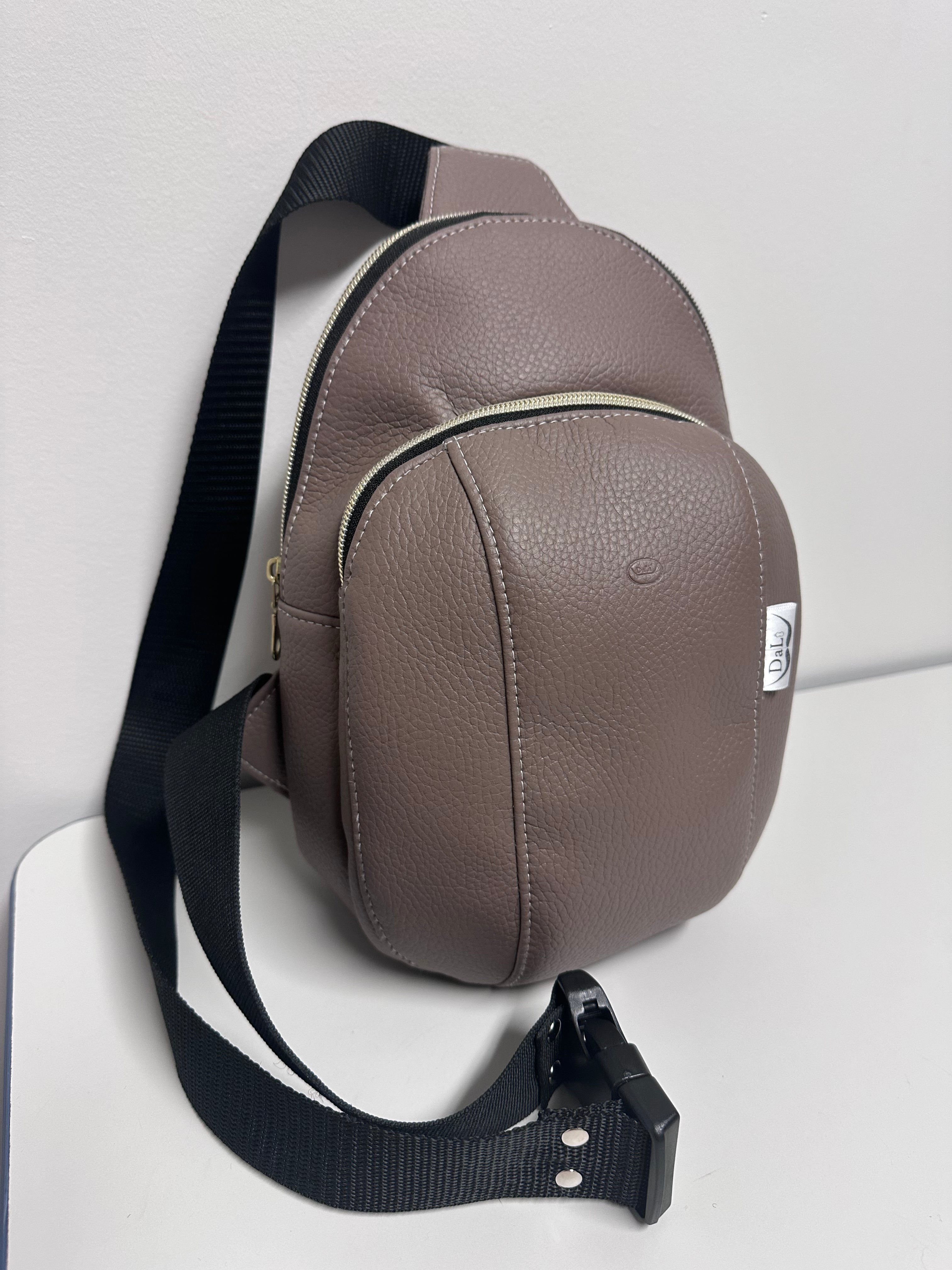 Brown leather sling bag with a visible brand logo on a light gray background