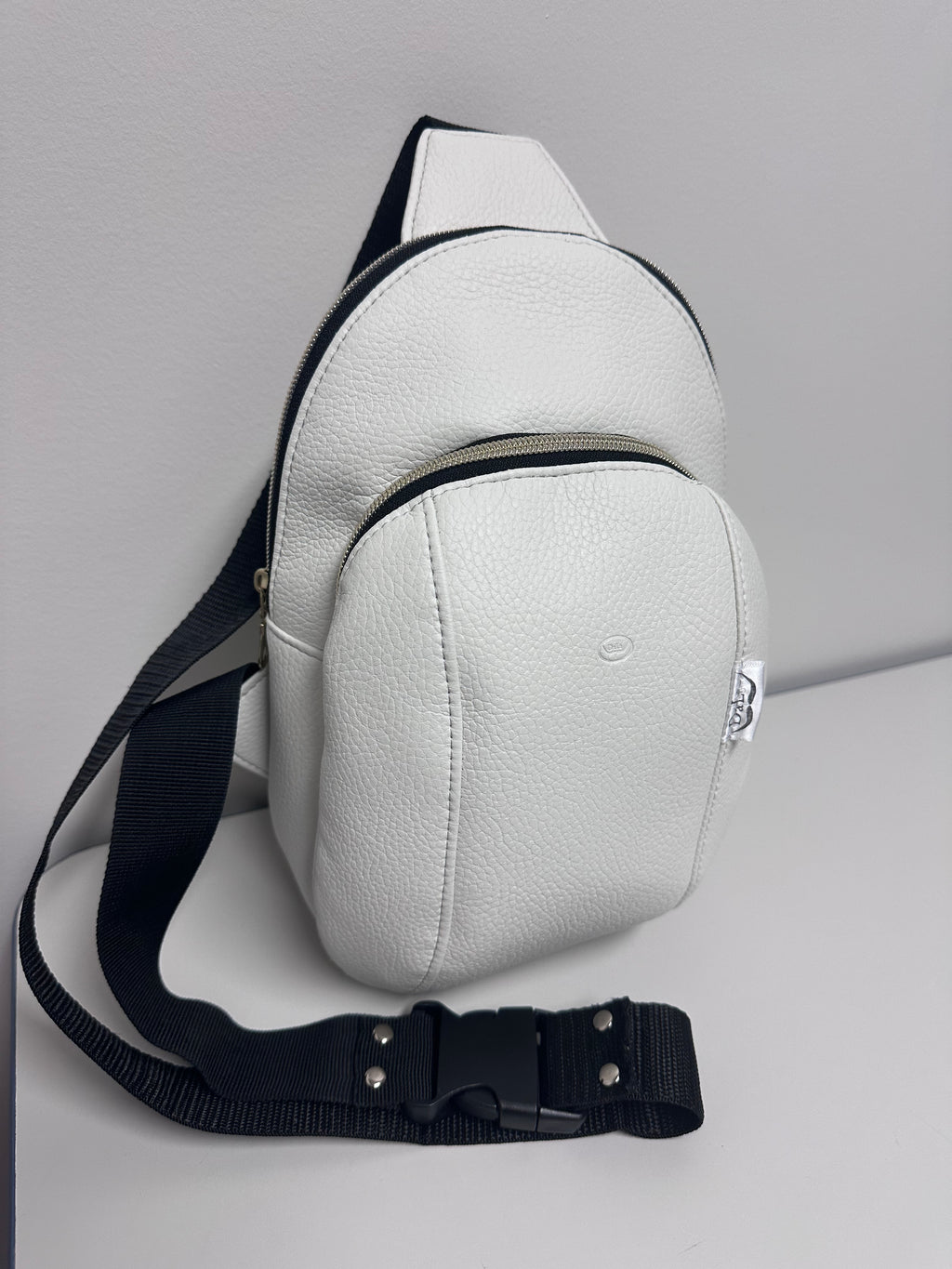 White leather sling bag with black strap on a light gray background