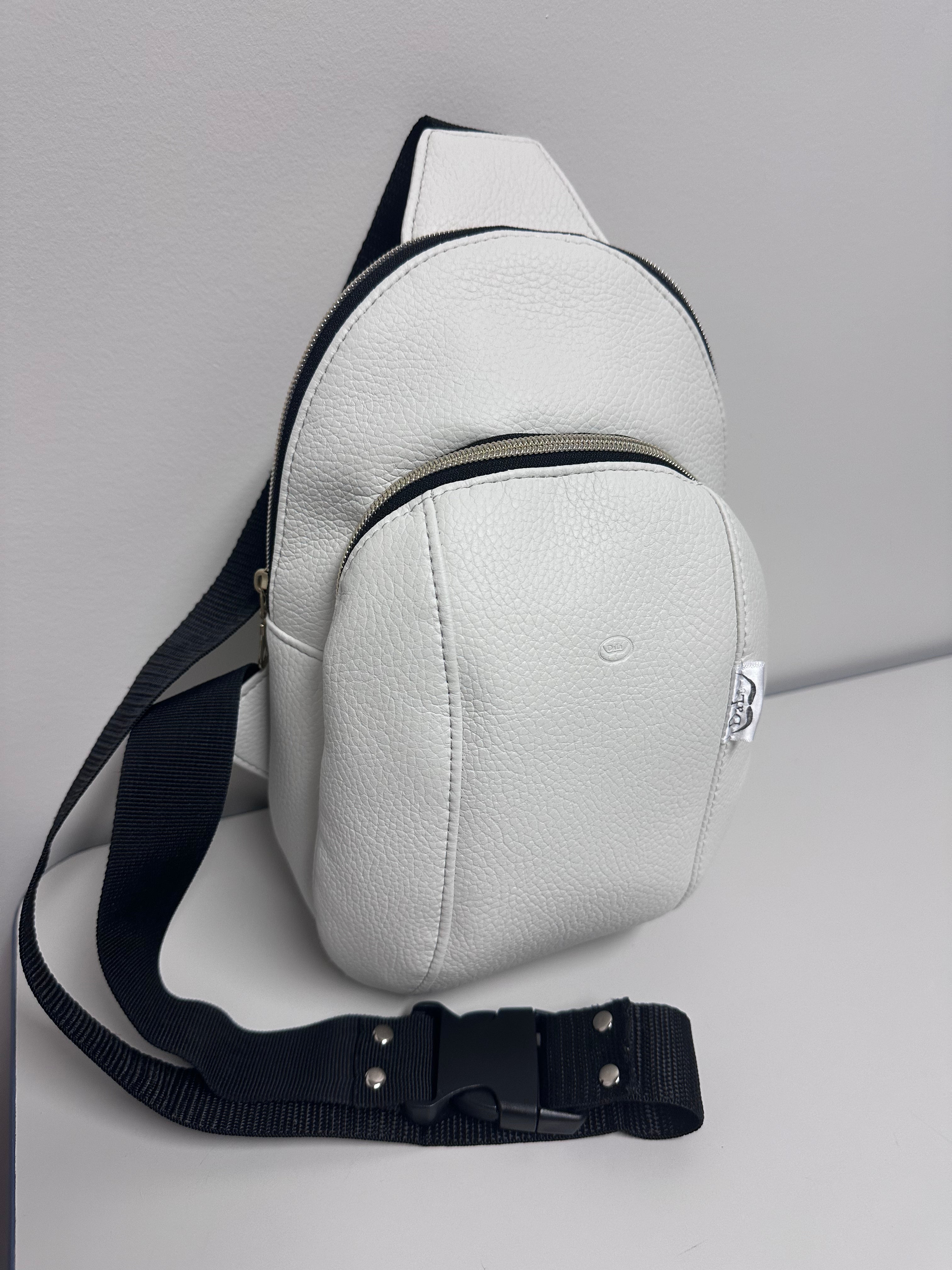 White leather sling bag with black strap on a light gray background