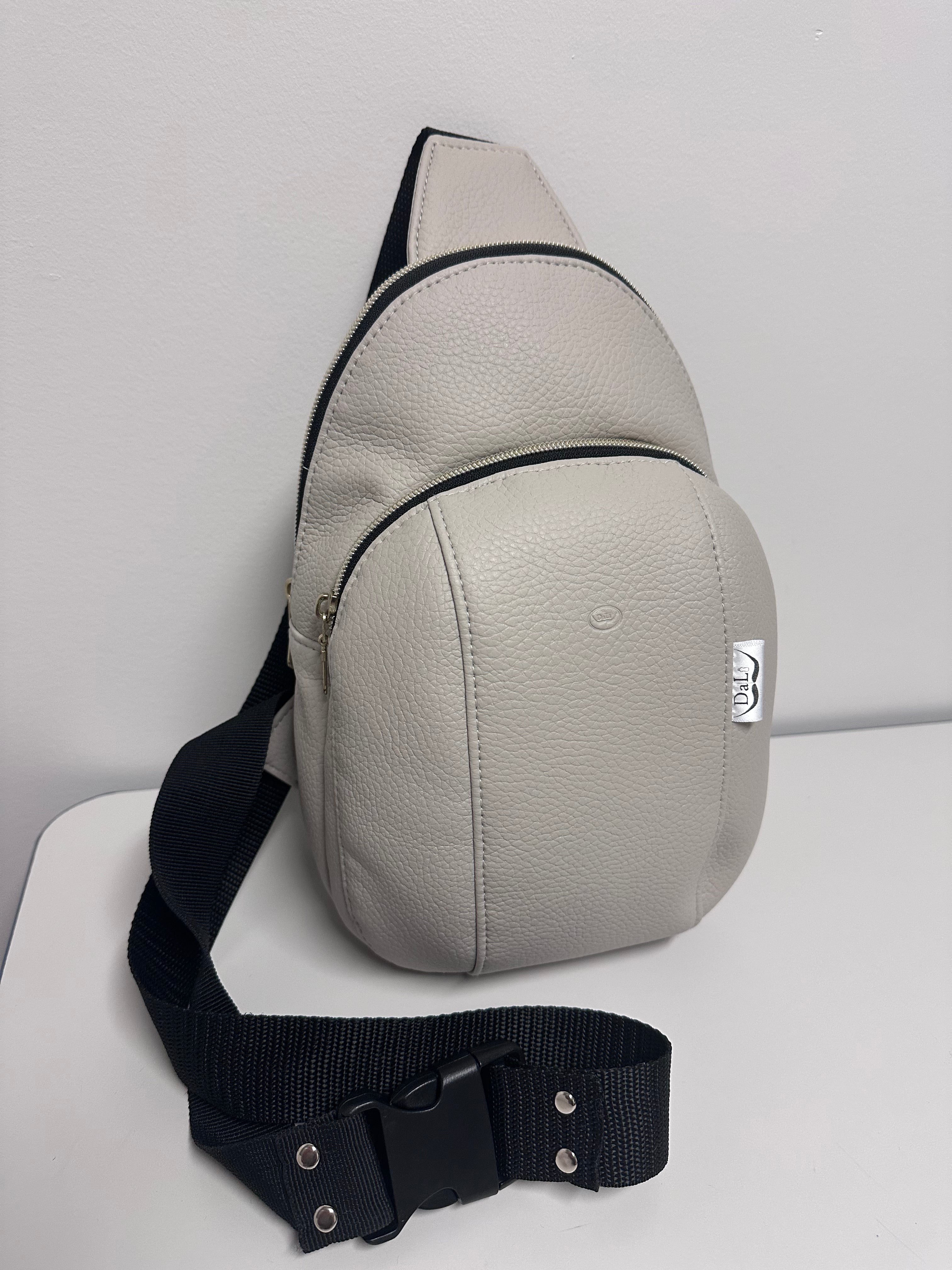 Gray sling bag with black strap on a light gray background