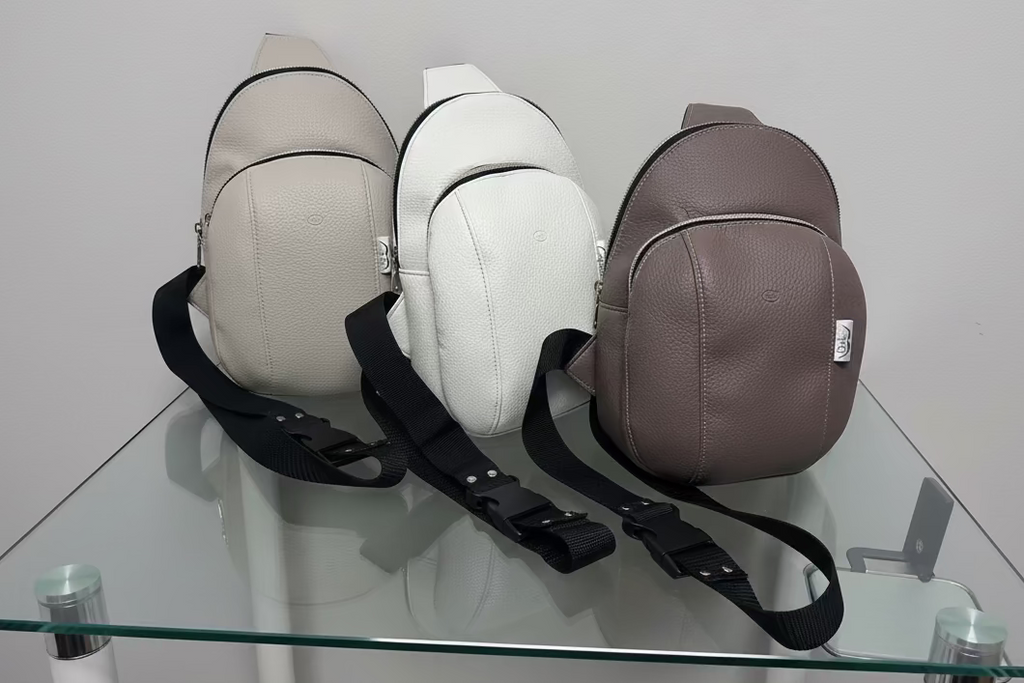 Three crossbody bags in beige, white, and brown on a glass surface with a white background