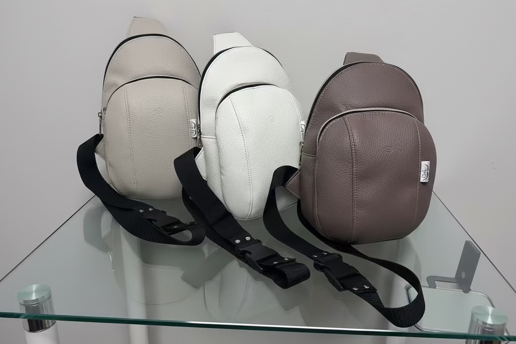 Three crossbody bags in beige, white, and brown on a glass surface with a white background