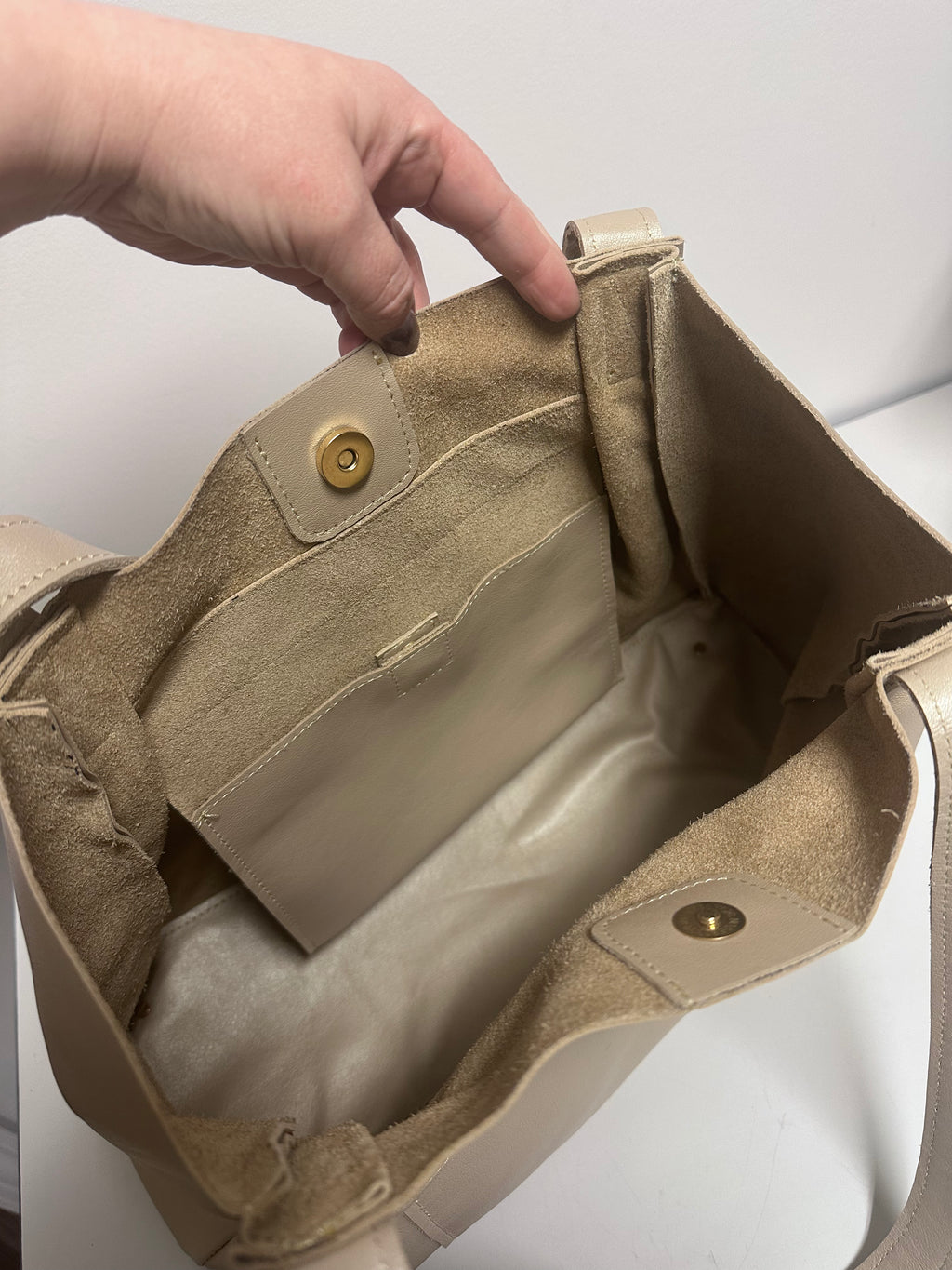 Beige handbag with gold hardware being held open by a hand on a white background