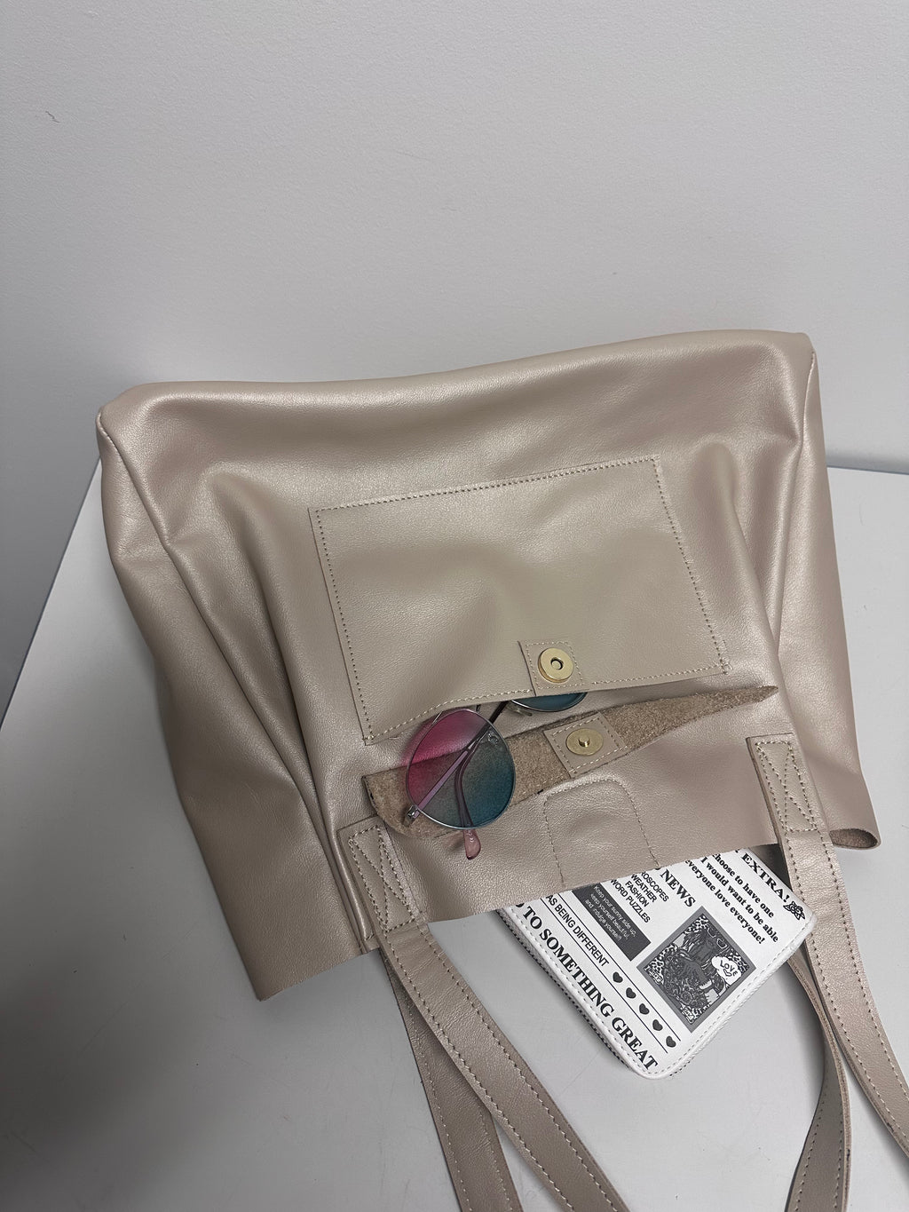 Beige genuine leather tote bag with sunglasses and a tag on a white surface