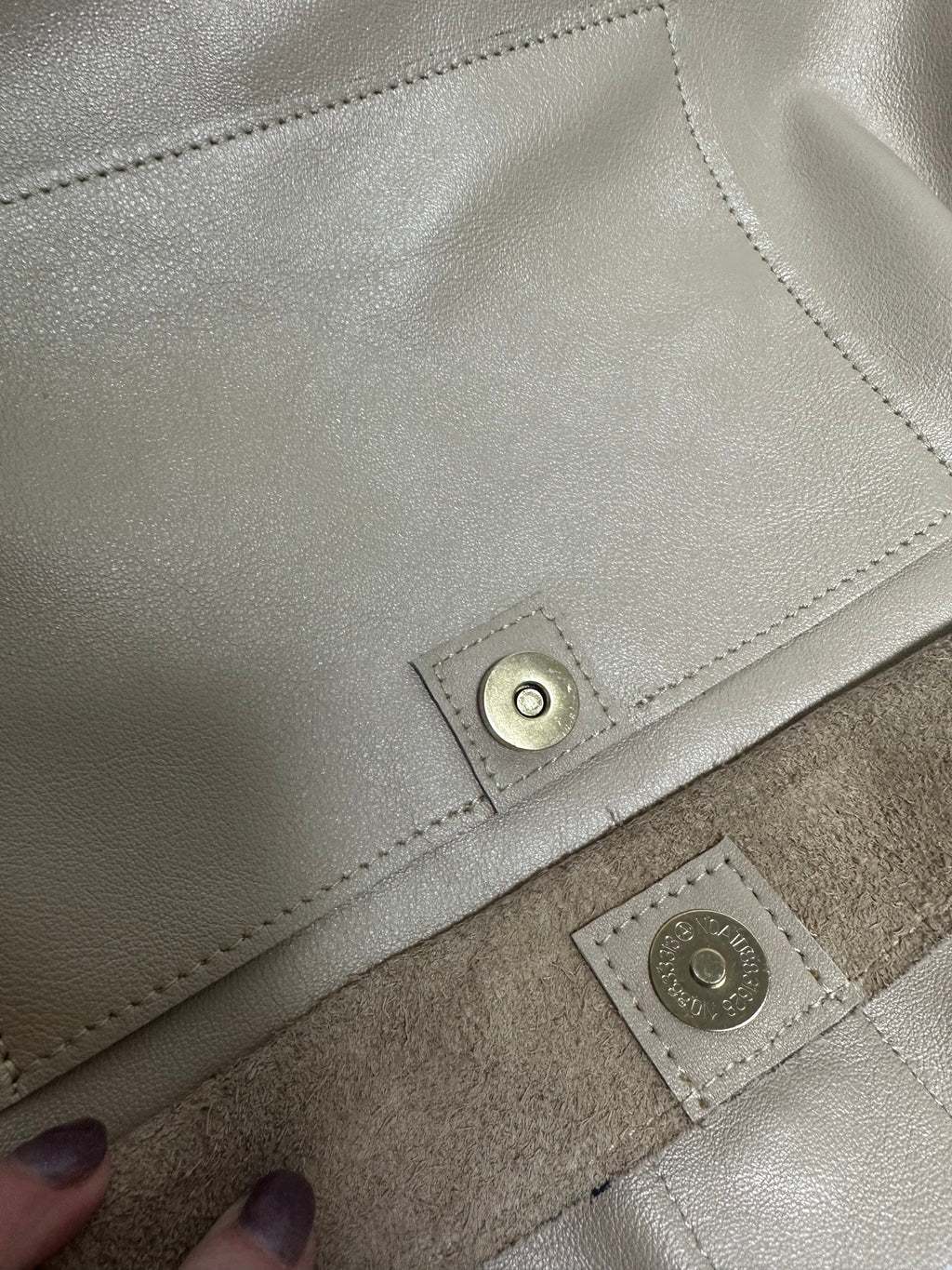 Close-up of a beige genuine leather bag with a gold button and brand label.