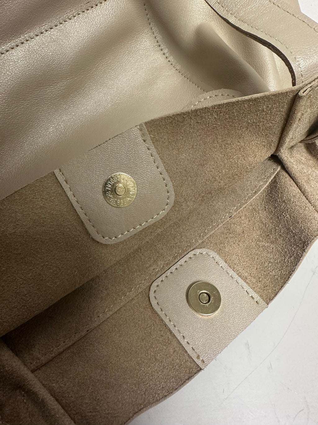 Close-up of a beige leather bag with gold buttons on a white background