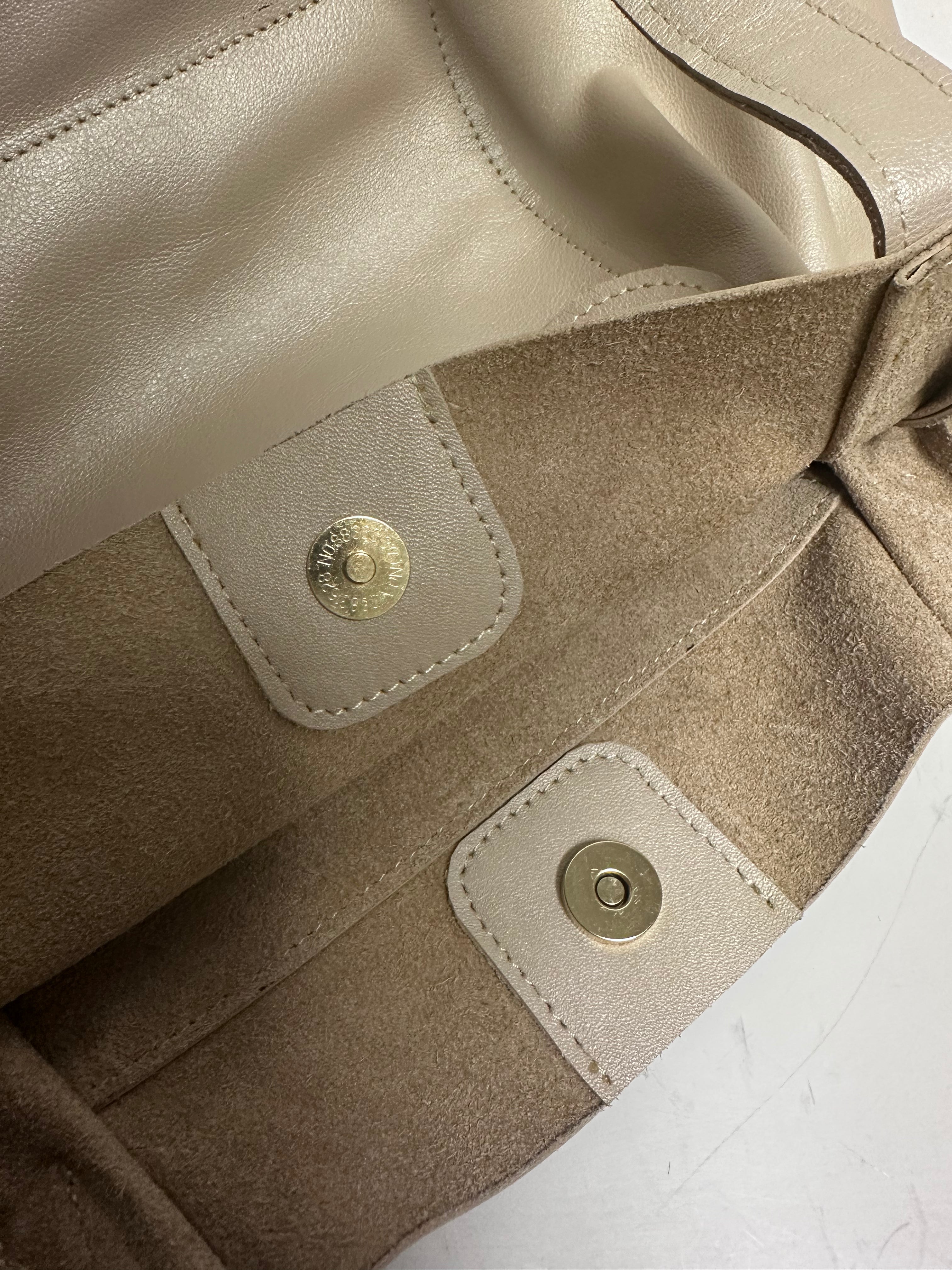 Close-up of a beige leather bag with gold buttons on a white background