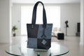 Black and gray tote bag on a glass table in a blurred indoor setting