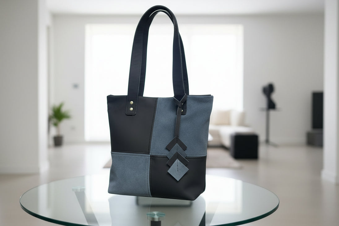 Black and gray tote bag on a glass table in a blurred indoor setting