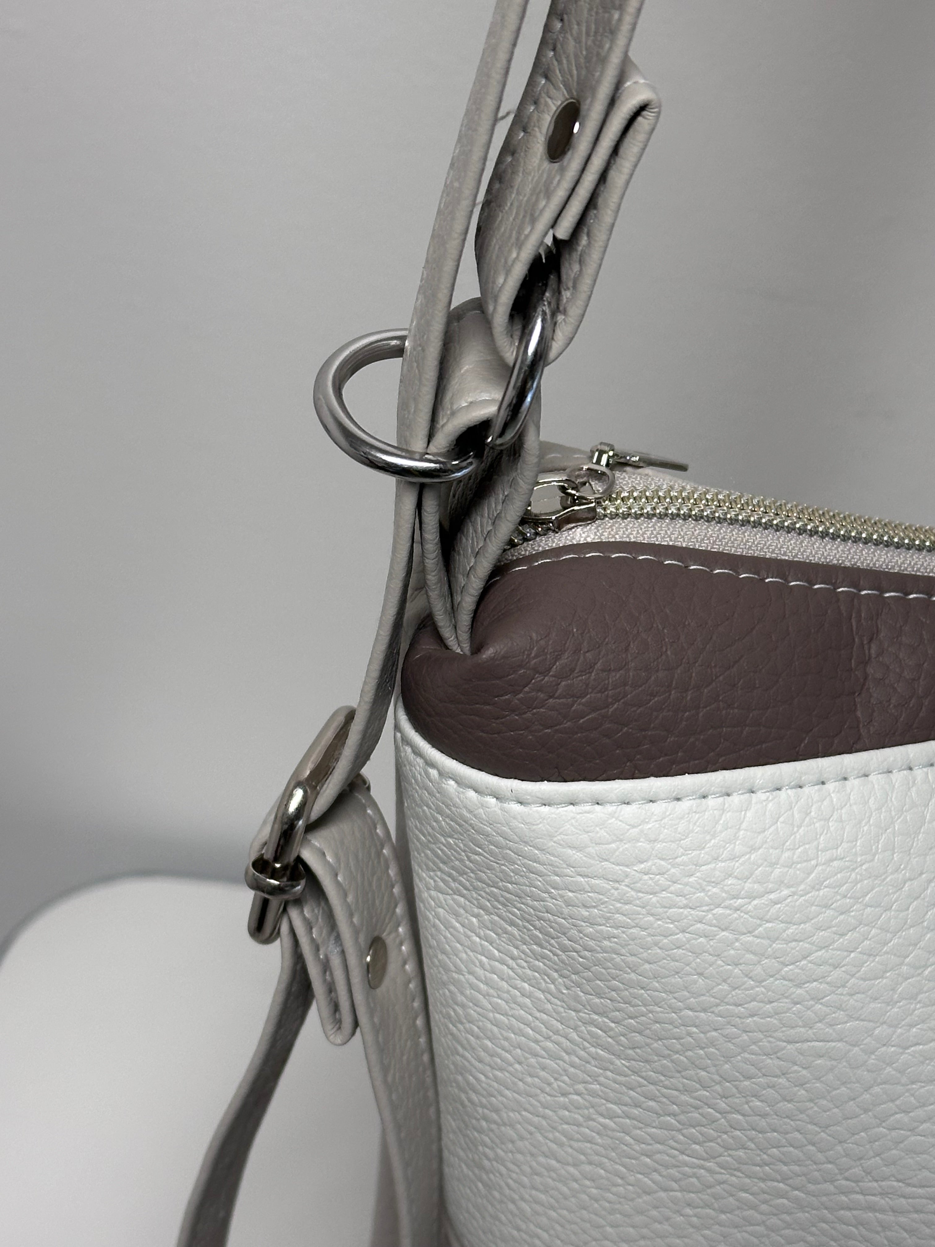 Close-up of a white leather handbag with a silver zipper and strap on a light gray background.