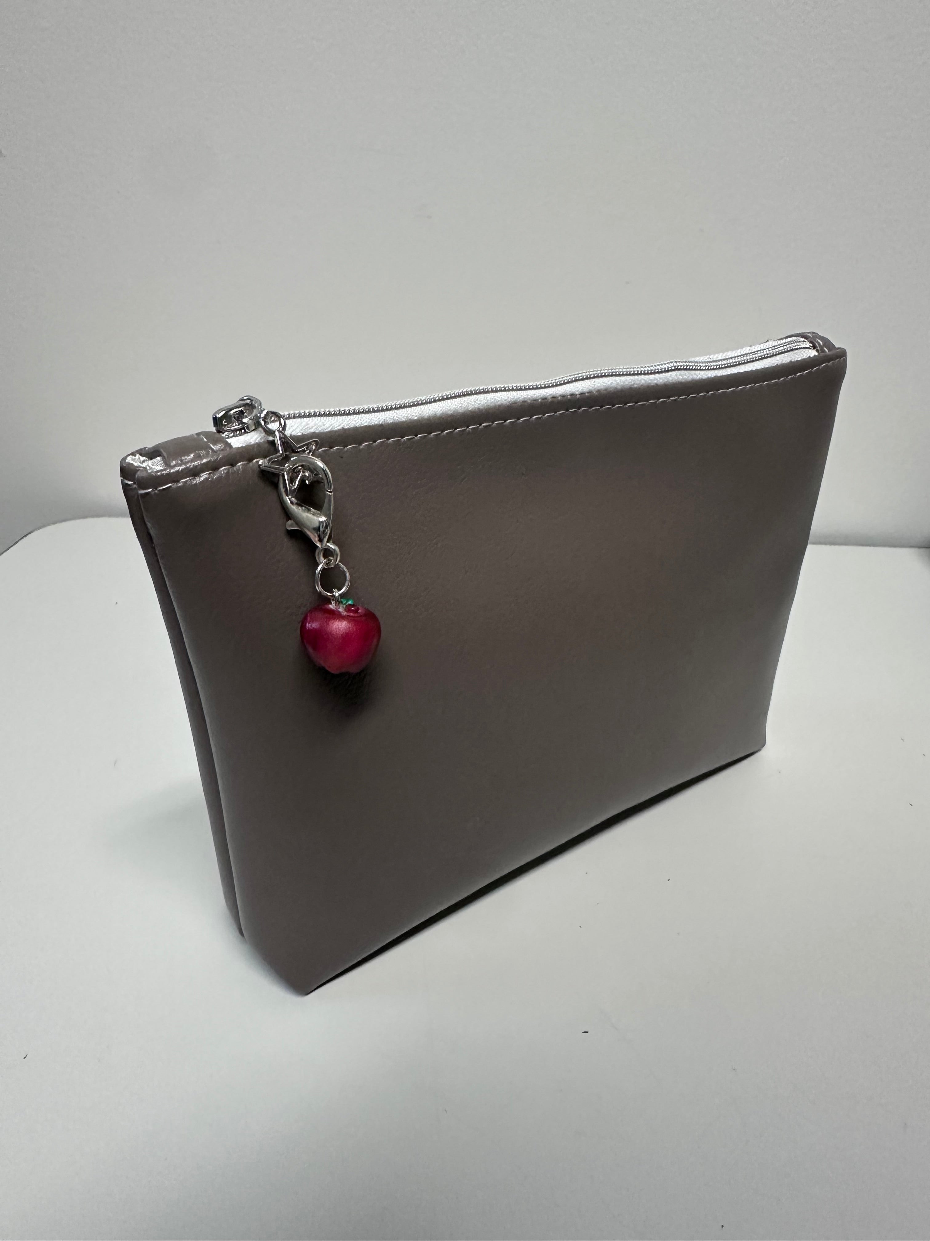 Gray clutch bag with a red charm on a white background