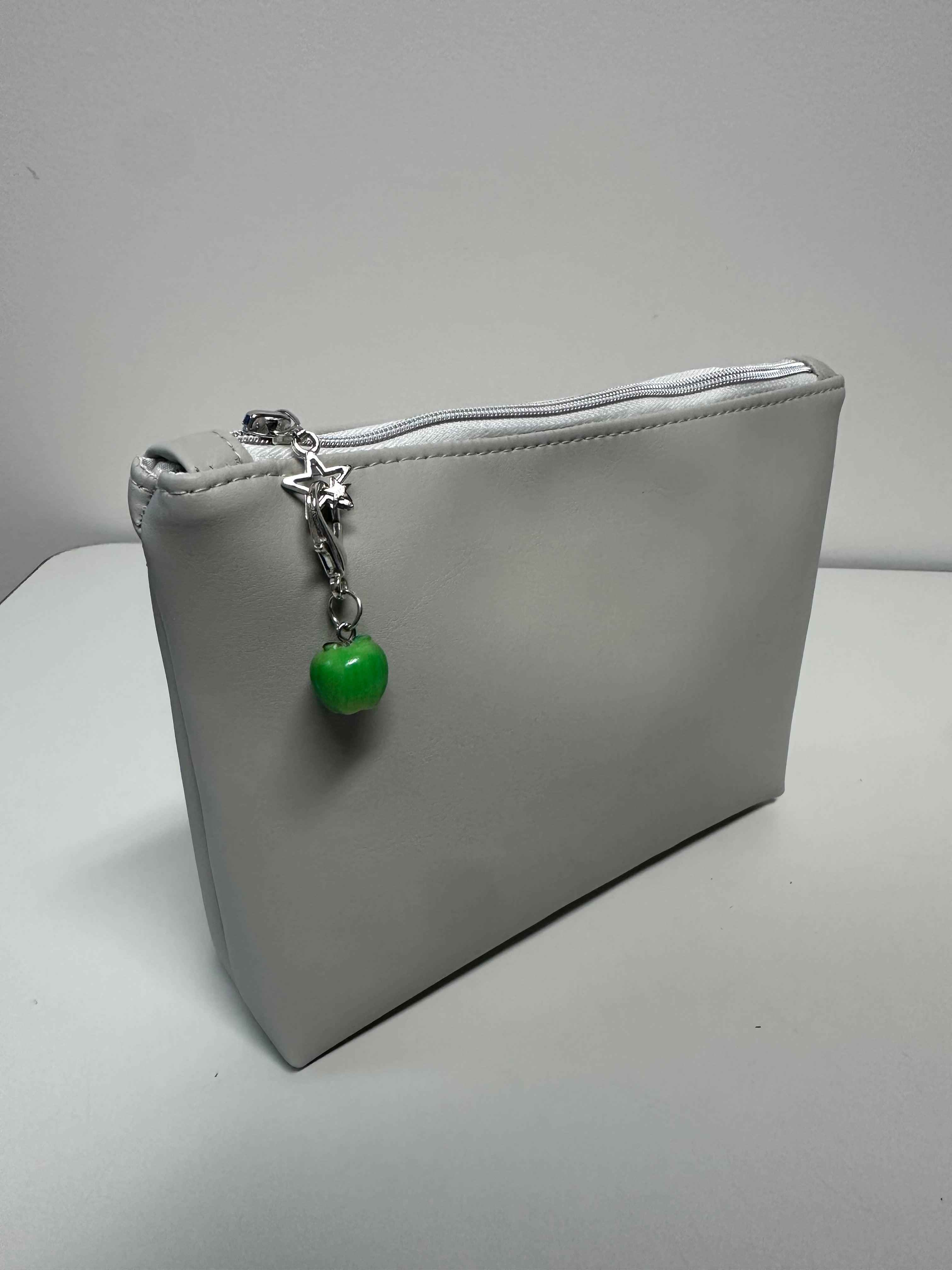 Gray clutch bag with a green bead charm on a white background