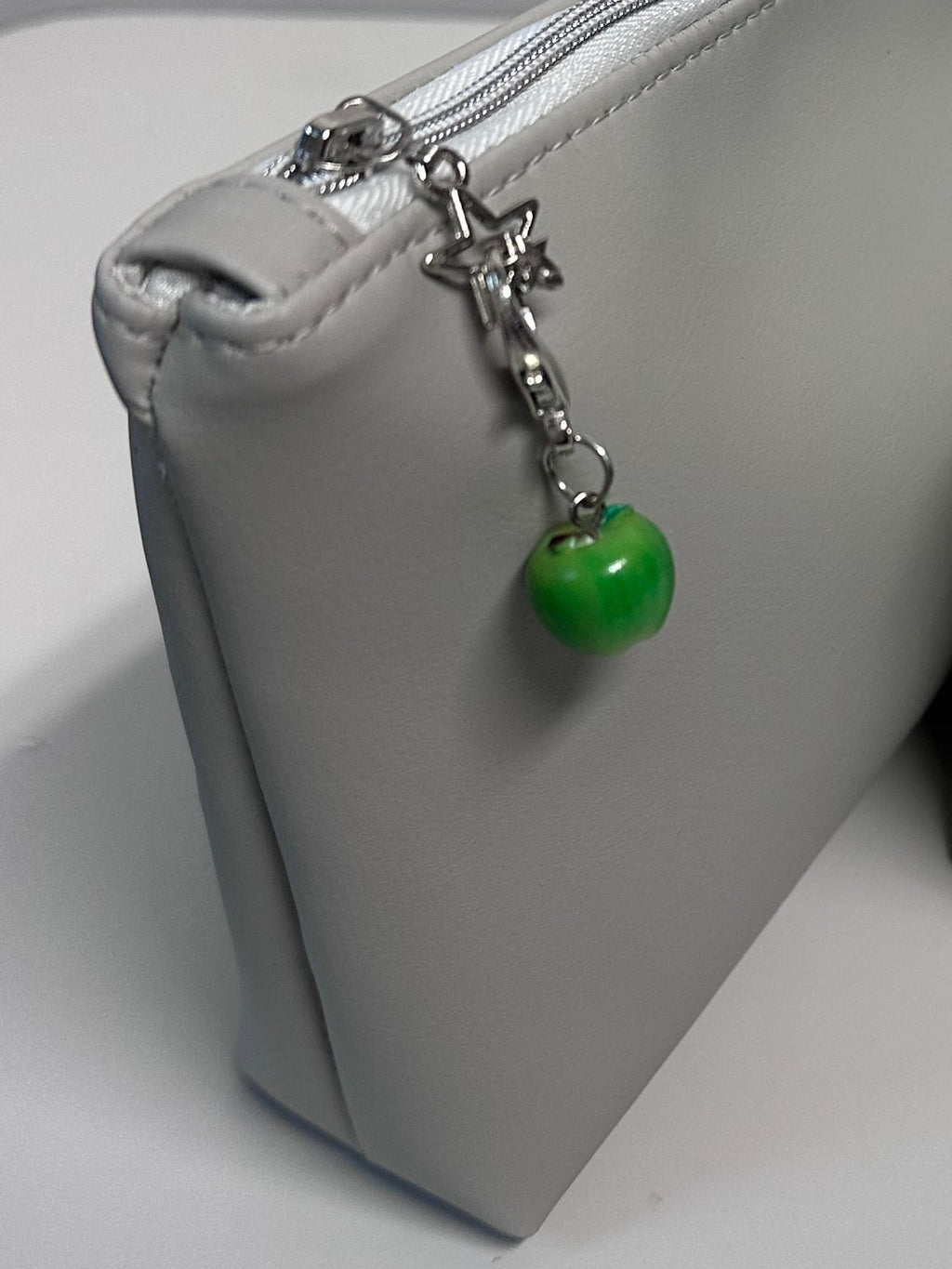 Close up view of light grey cosmetic bag with green apple charm