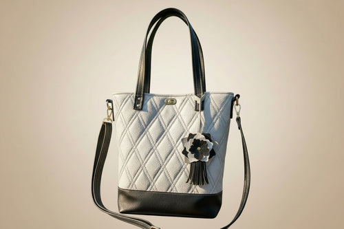 White handbag with black accents and a decorative flower on a light gray background