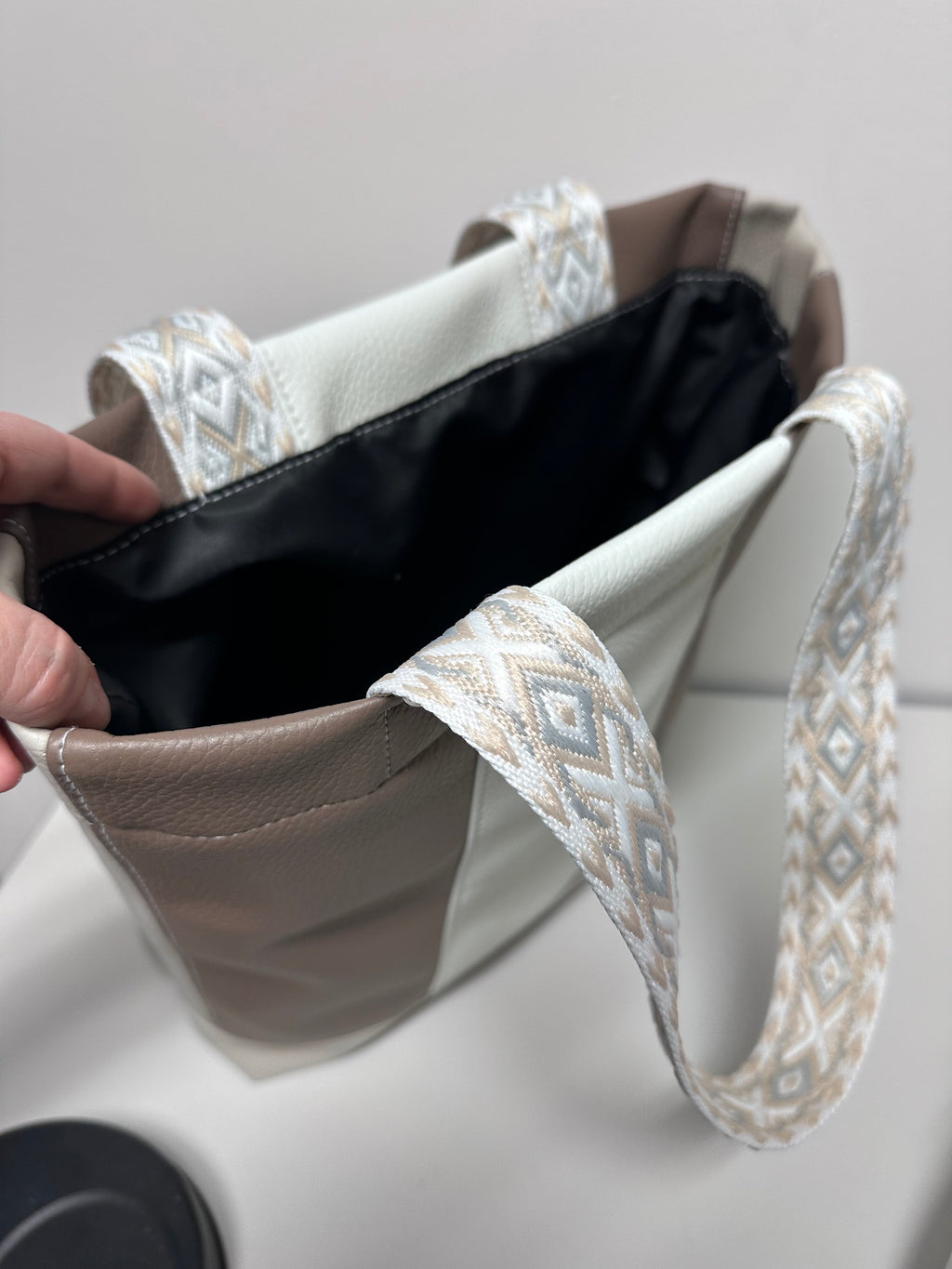Close-up of a hand holding a folded handmade bag with a decorative pattern against a neutral background
