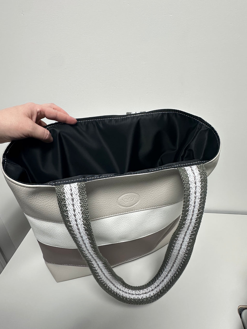 Hand holding a stylish handbag with a visible brand logo against a neutral background