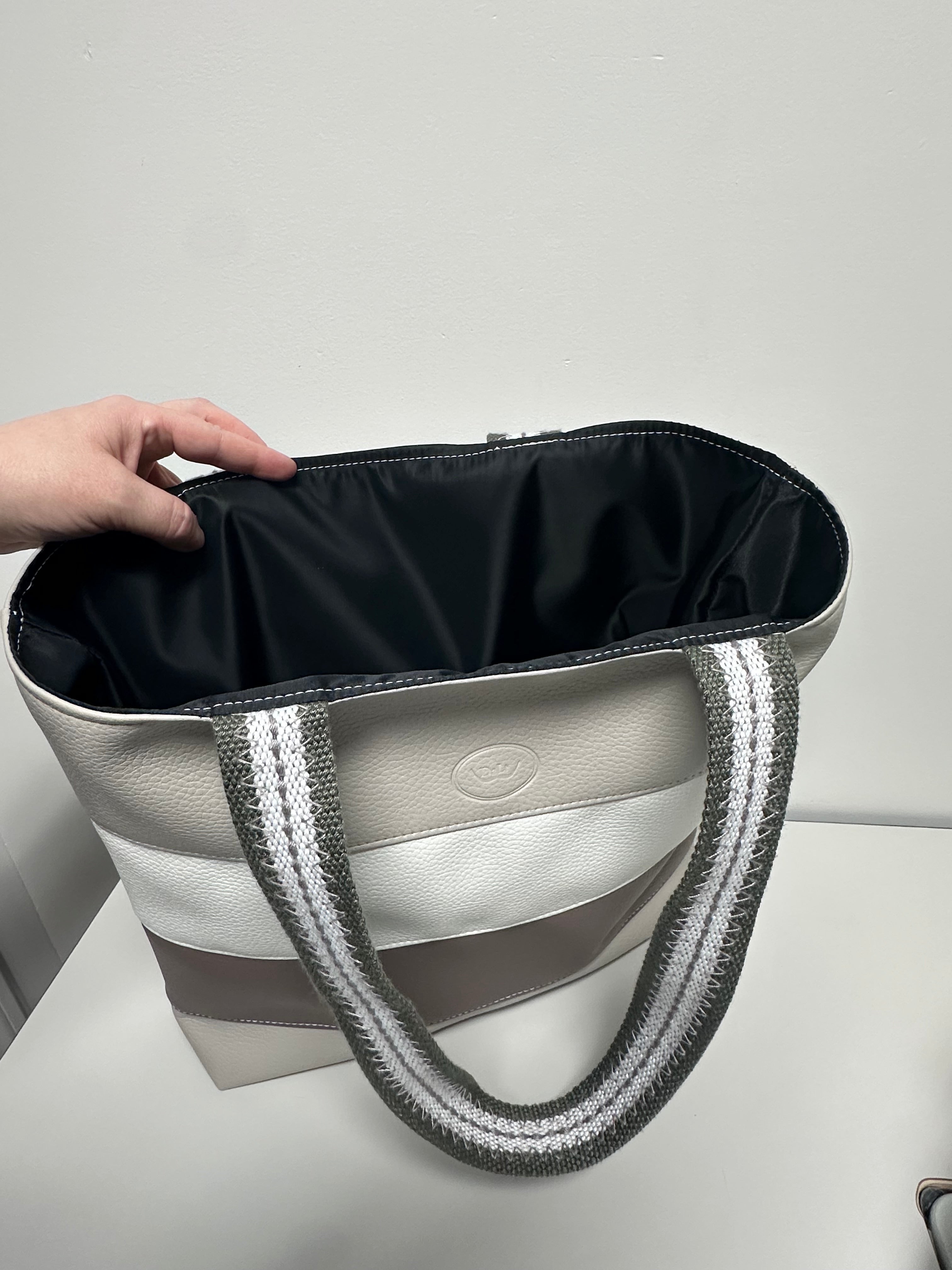 Hand holding a stylish handbag with a visible brand logo against a neutral background