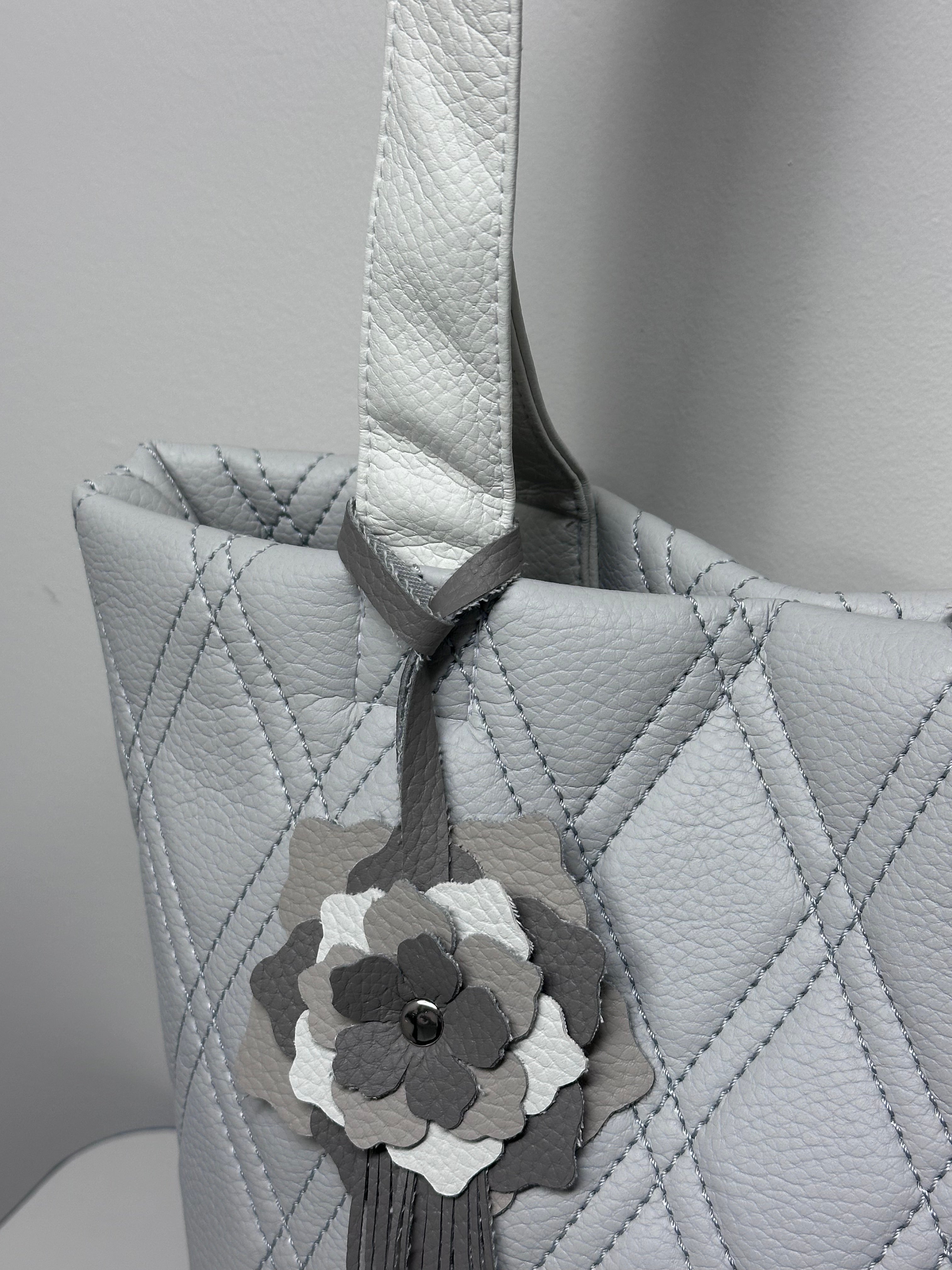 Gray quilted handbag with a floral accessory on a light gray background