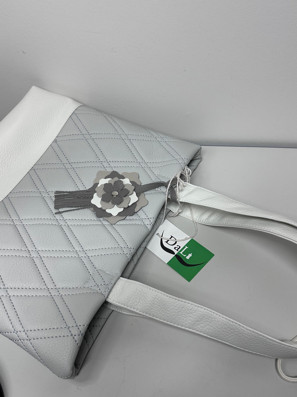 Gray quilted handbag with a floral tag on a light gray background