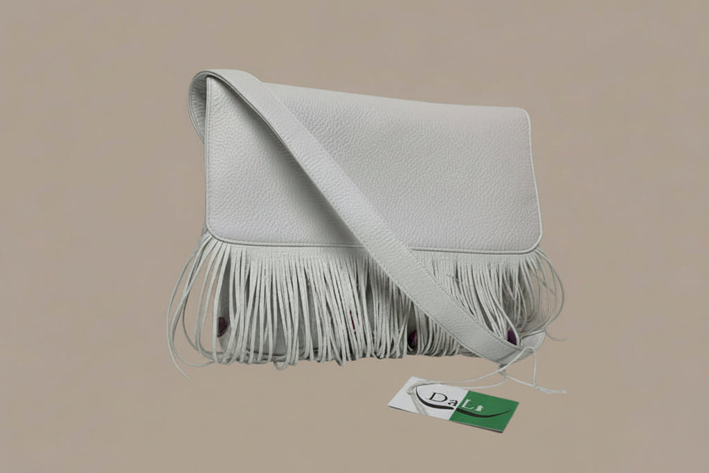 White handbag with fringe details on a reflective surface with a gray background
