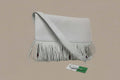 White handbag with fringe details on a reflective surface with a gray background