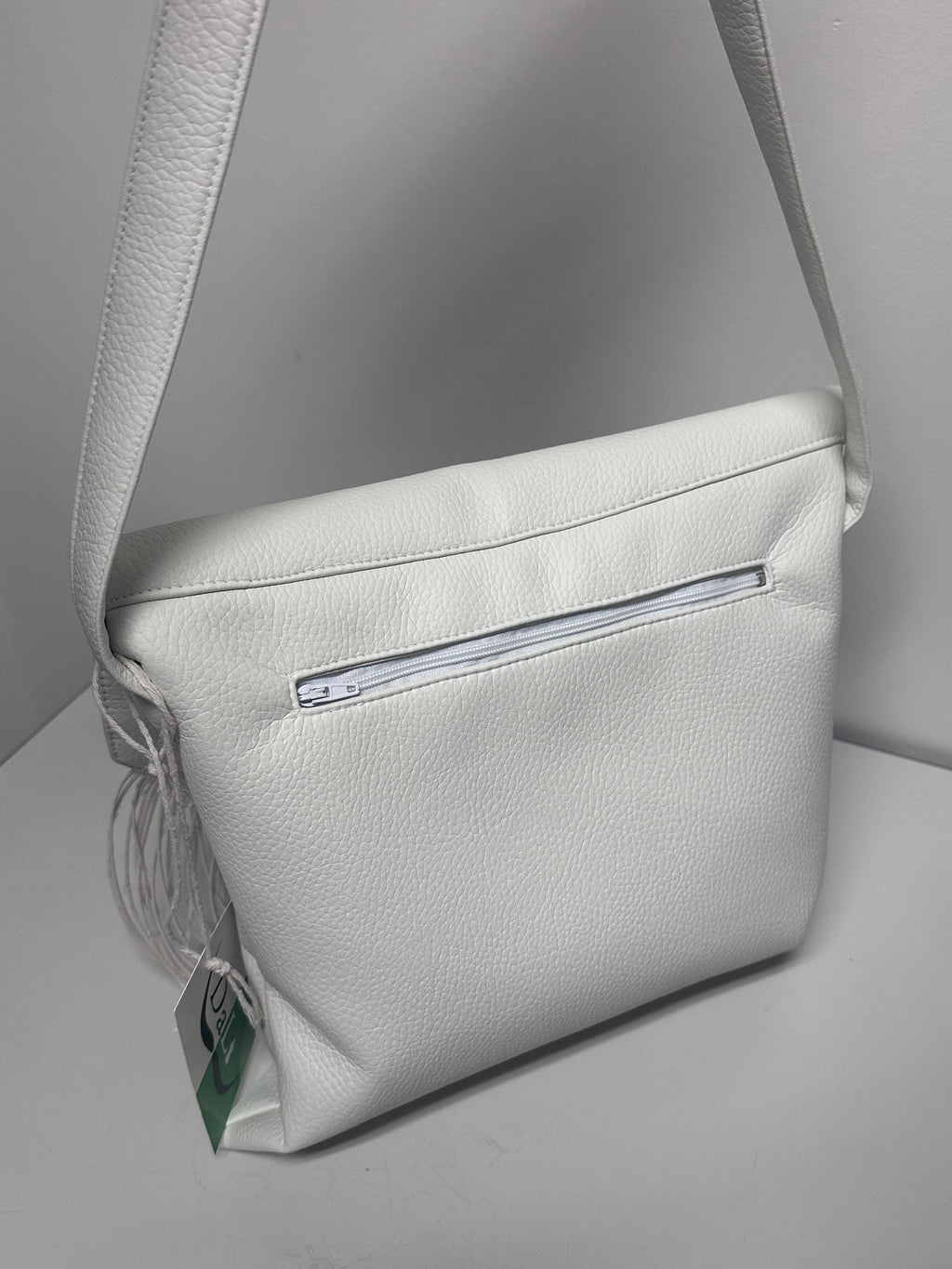 White faux leather handbag with a visible brand label on a light gray background