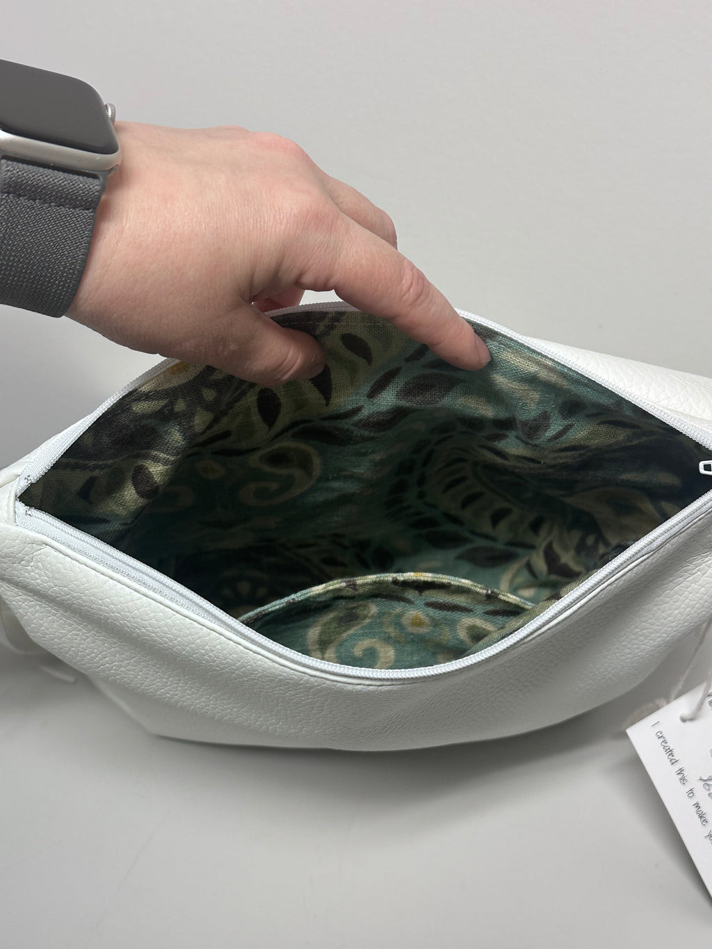 Hand opening a white bag with a patterned interior on a light gray background