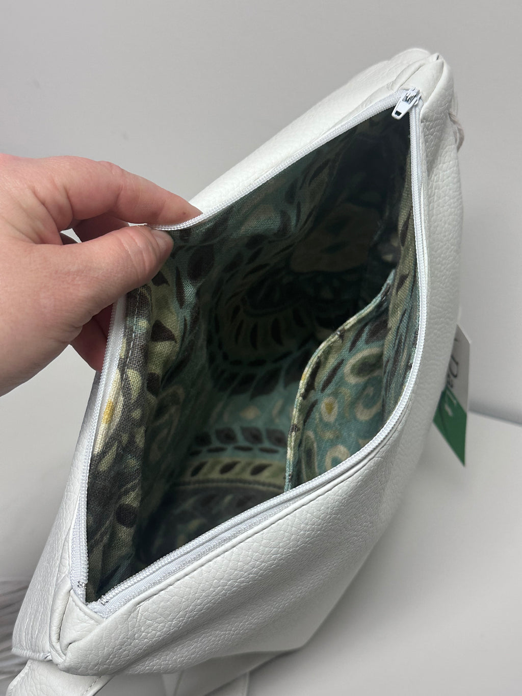 Hand holding a white bag with a patterned interior against a neutral background