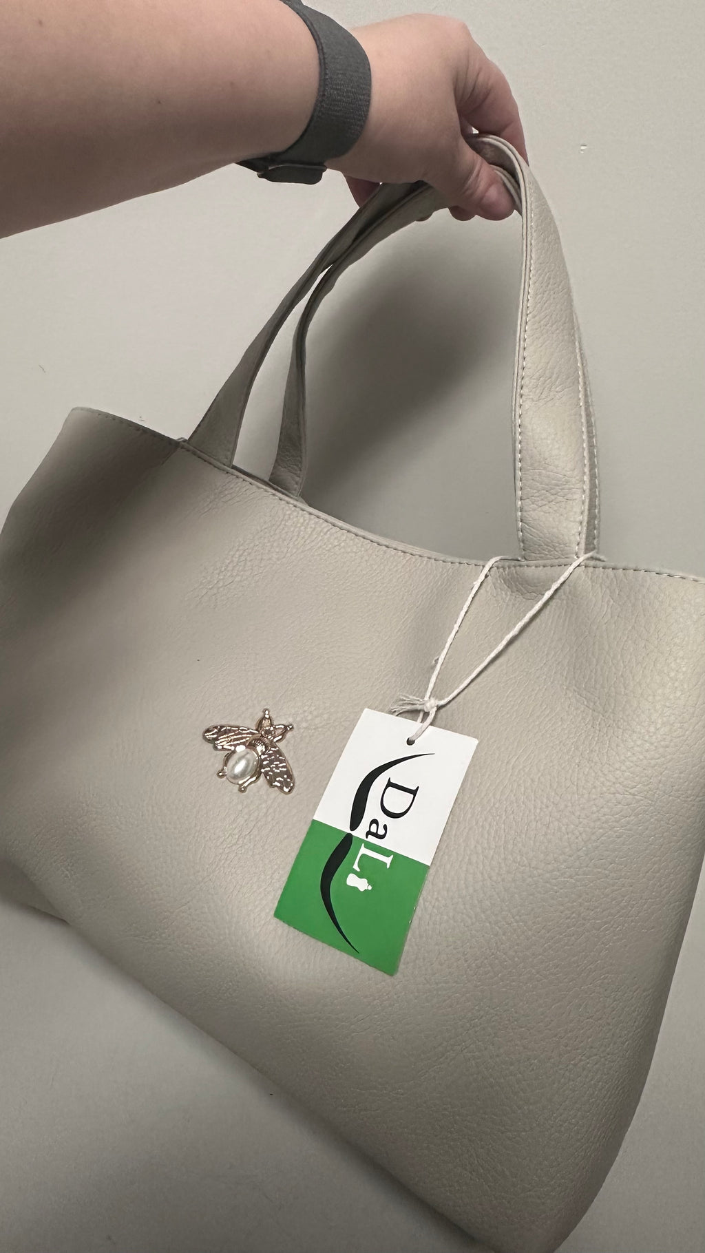 Beige handbag with a brand tag featuring a bee logo on a neutral background