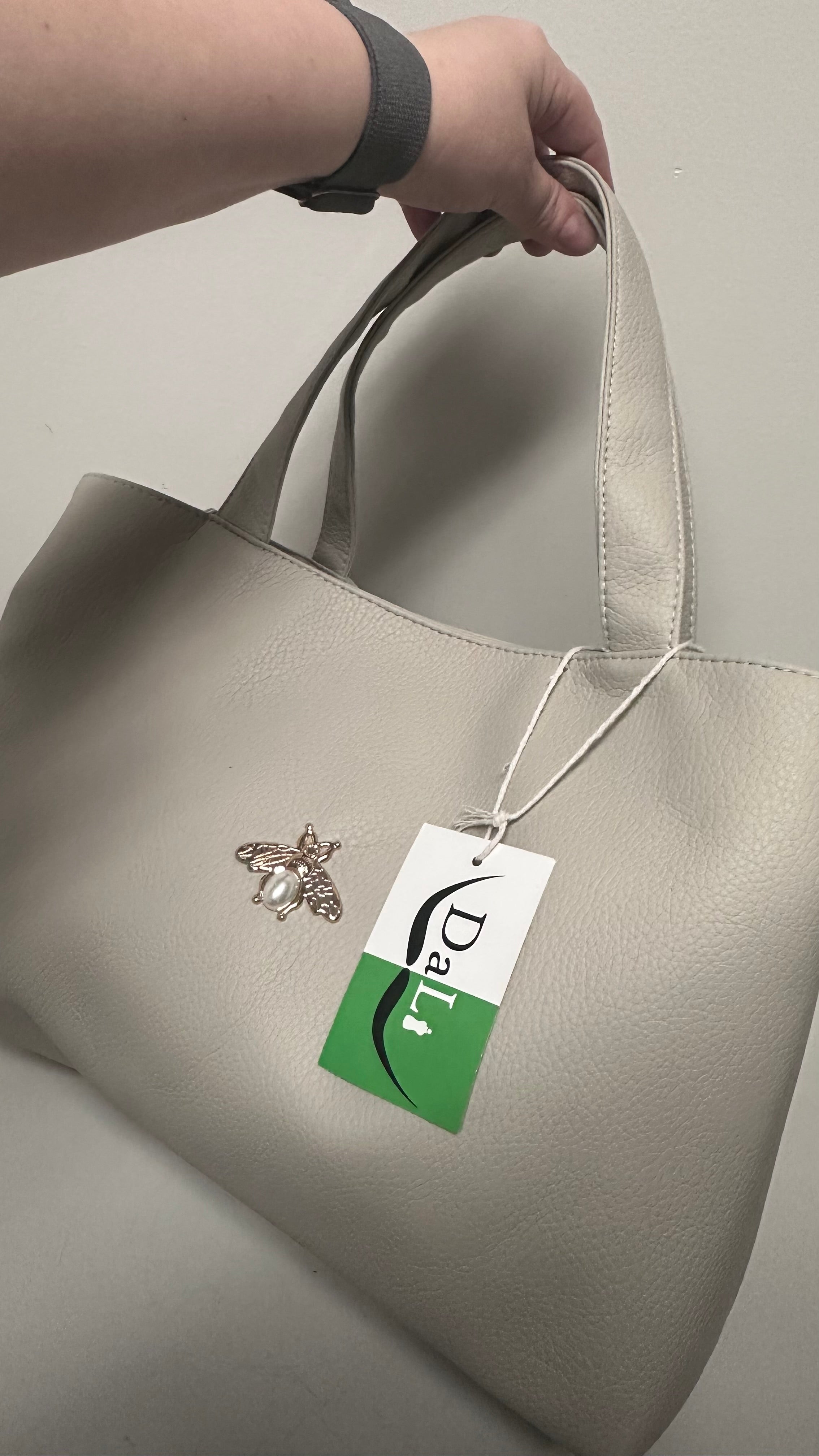 Beige handbag with a brand tag featuring a bee logo on a neutral background