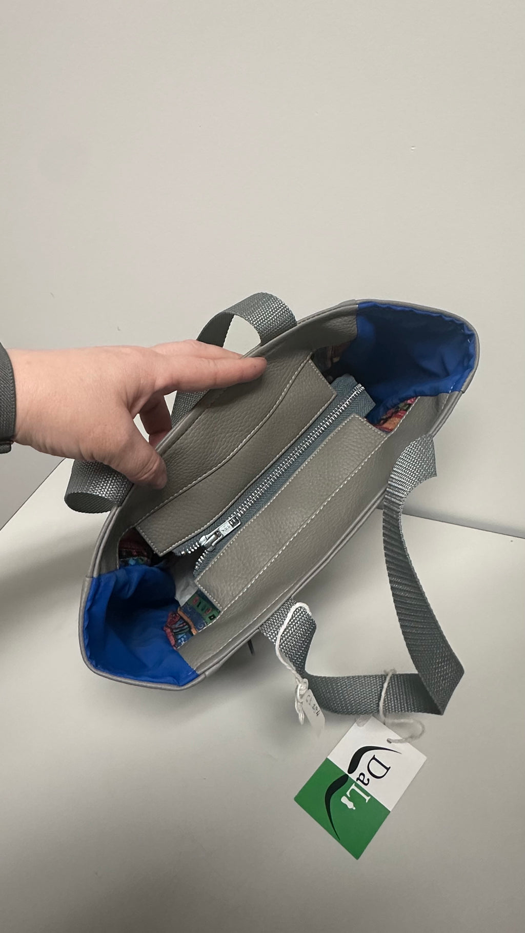 Gray bag with blue interior held by a hand on a light gray background