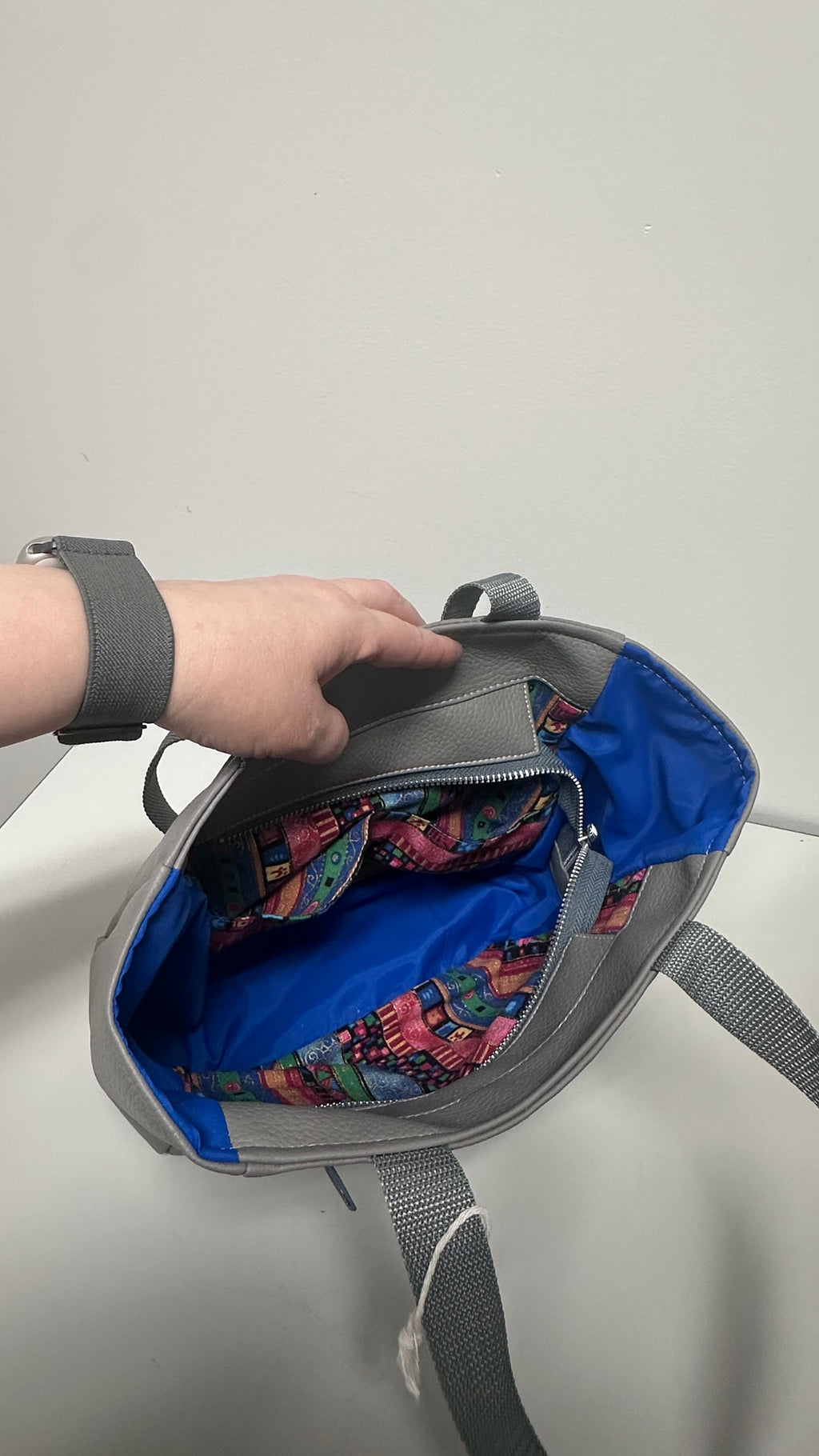 Gray bag with colorful interior being held open by a hand on a light gray background