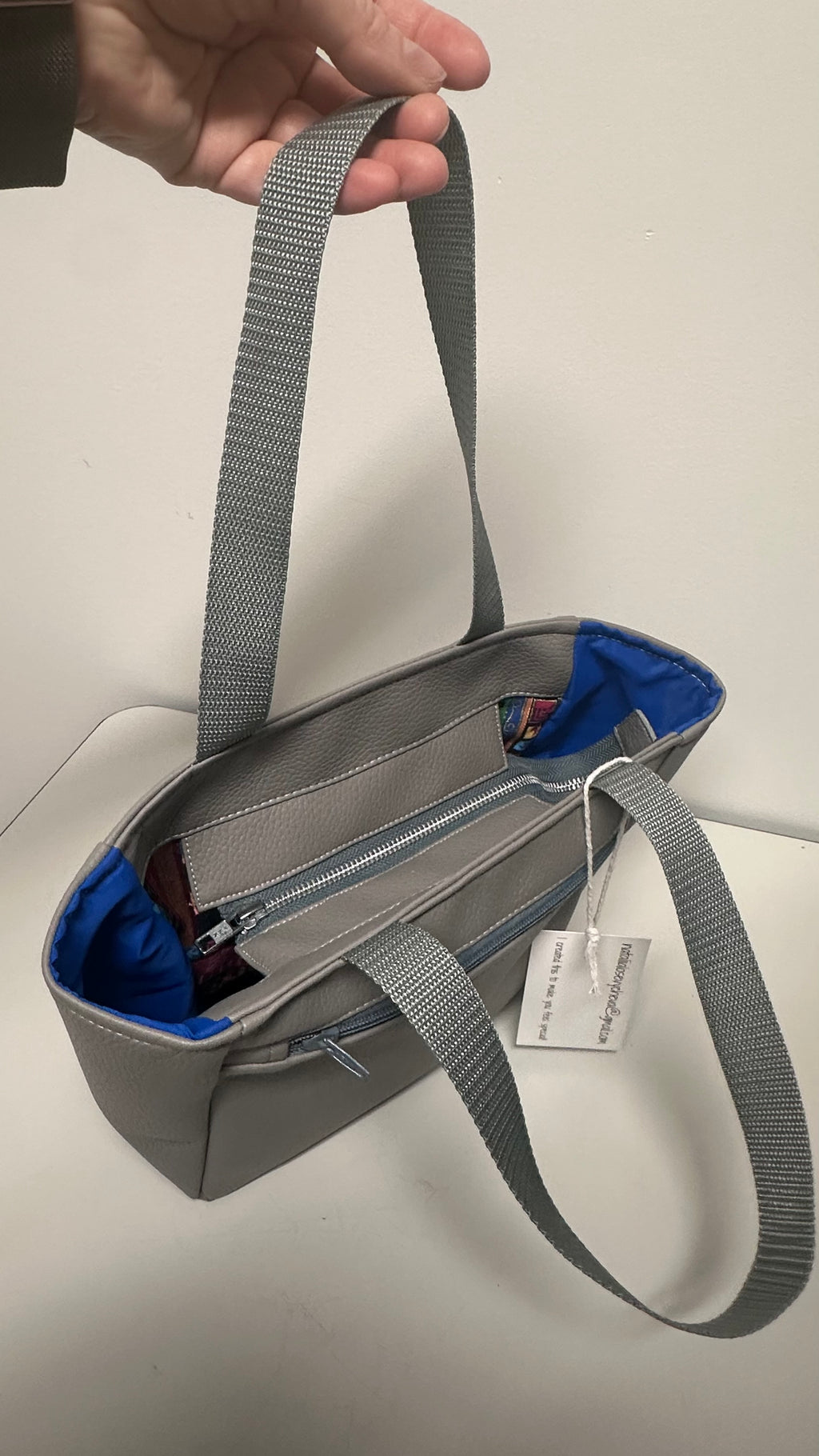 Gray handbag with a blue interior held by a hand on a light gray background