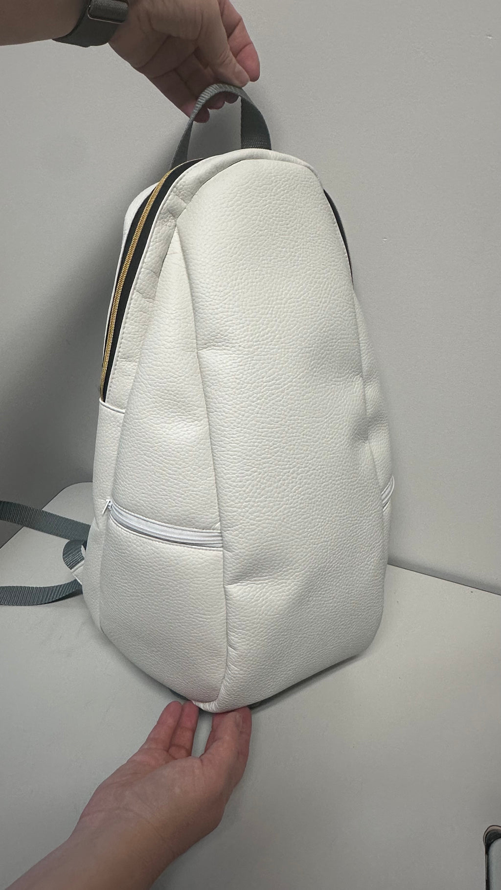 White textured backpack held by a person on a light gray background