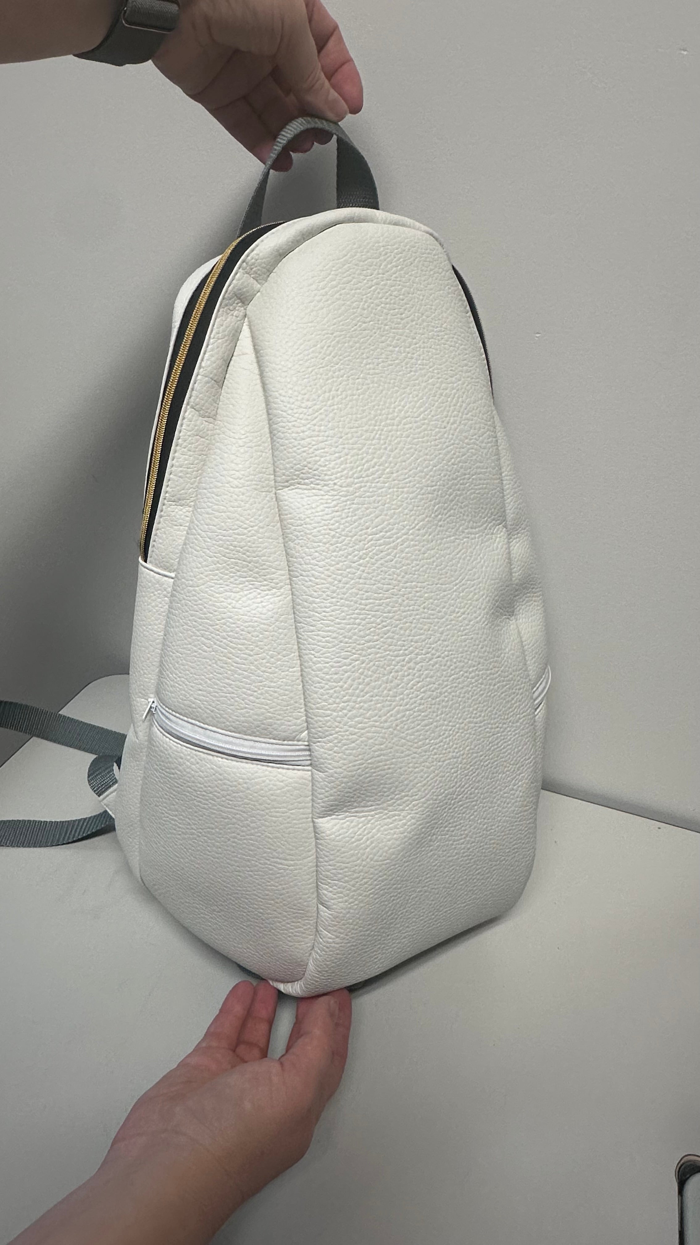 White textured backpack held by a person on a light gray background