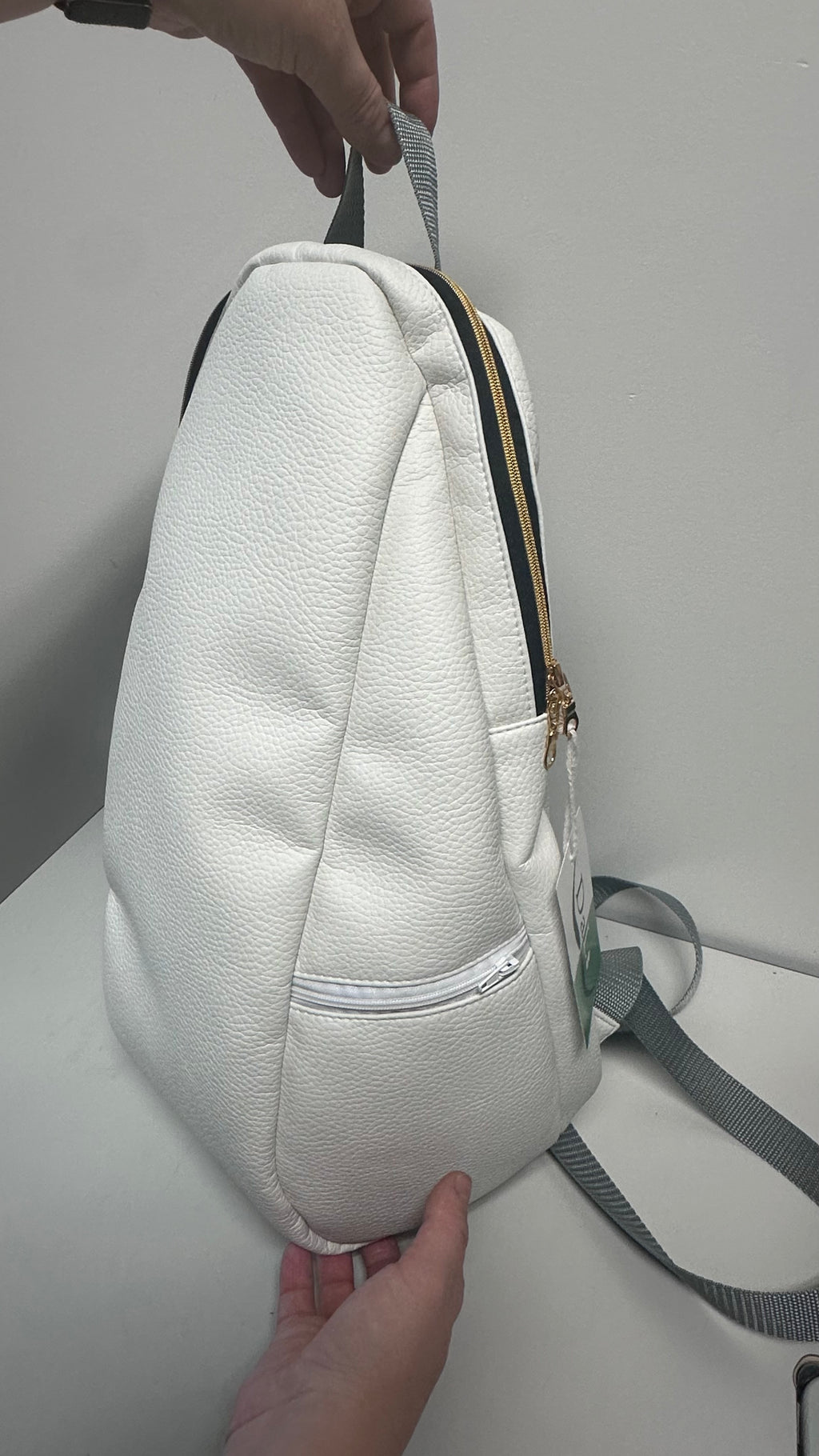 White textured backpack held by a person on a light gray background