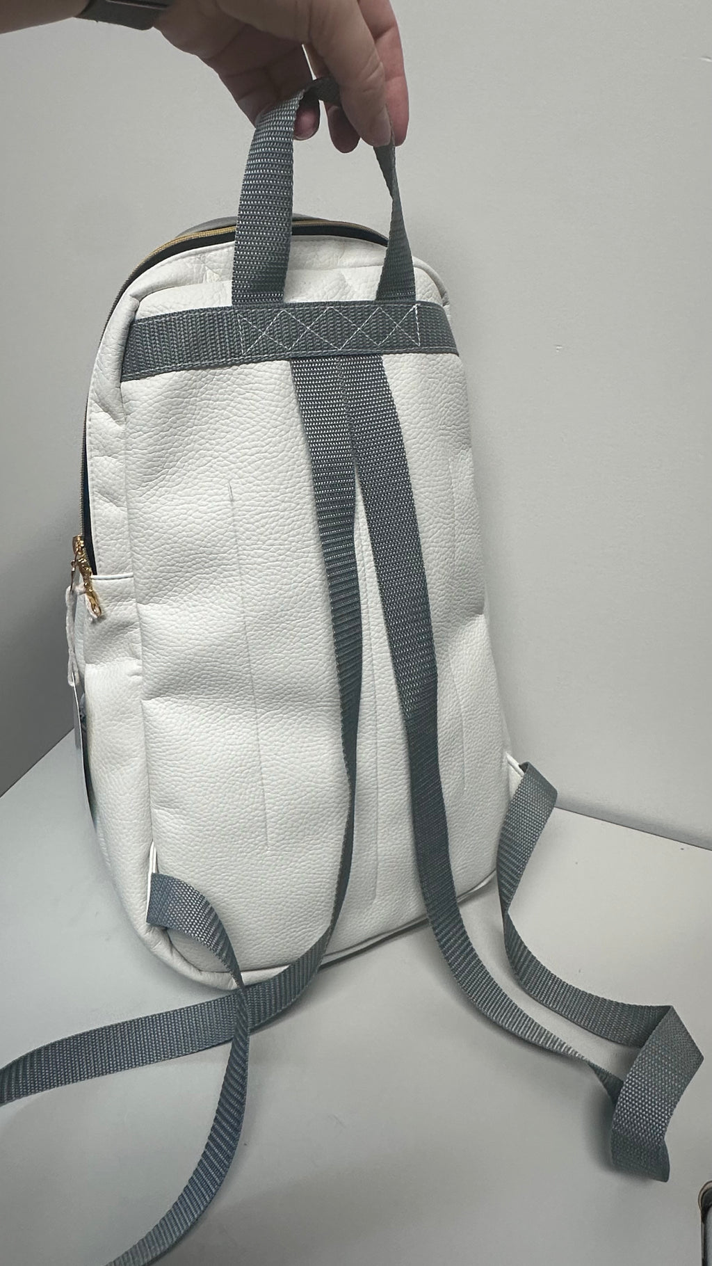 White backpack with gray straps held by a hand on a light gray background