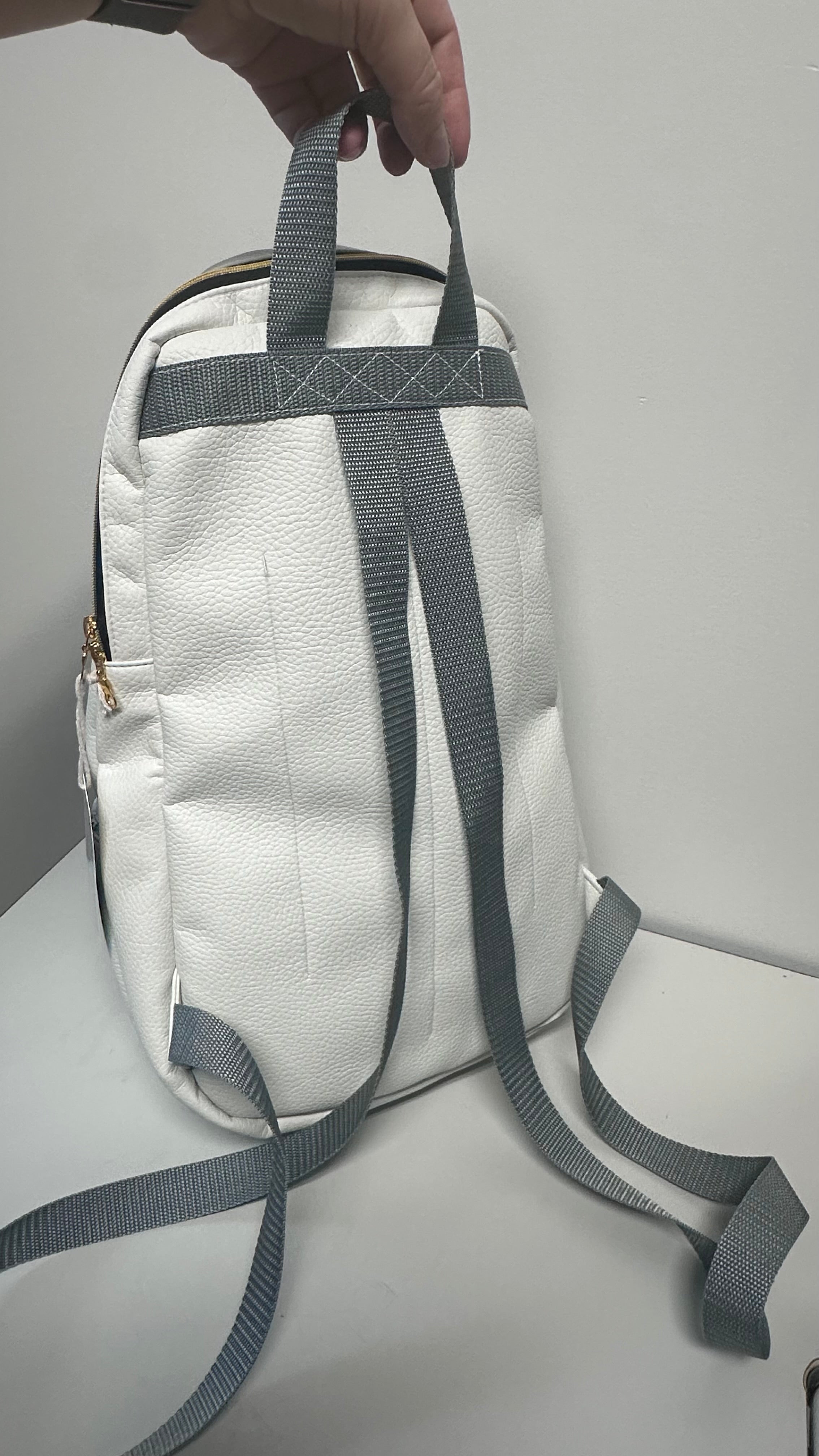 White backpack with gray straps held by a hand on a light gray background