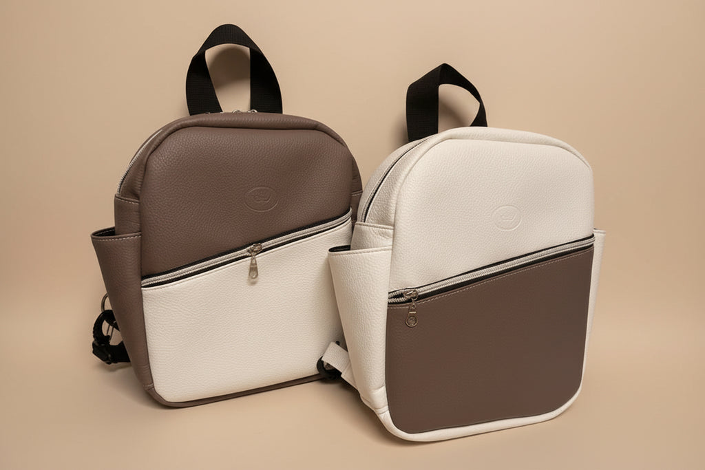 Two backpacks, one white and one tan, on a light gray surface.